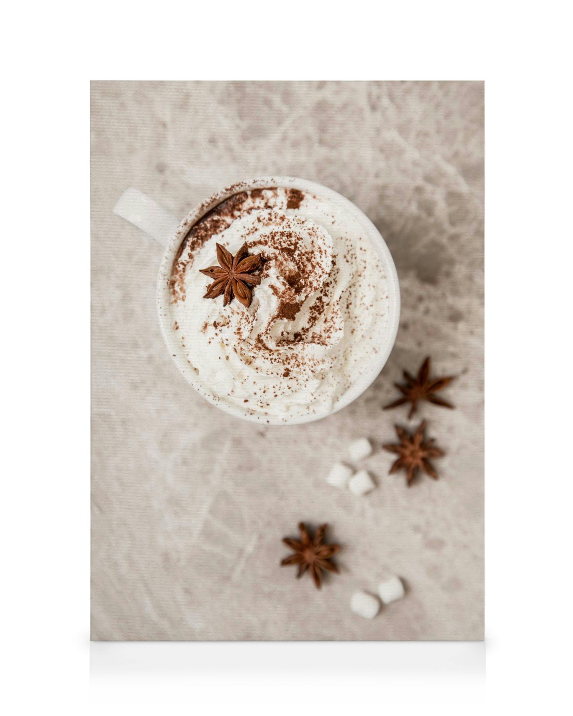 Varm choklad med vispgrädde, kakaopulver, marshmallows och stjärnanis, fotograferad ovanifrån på en marmorbänk.