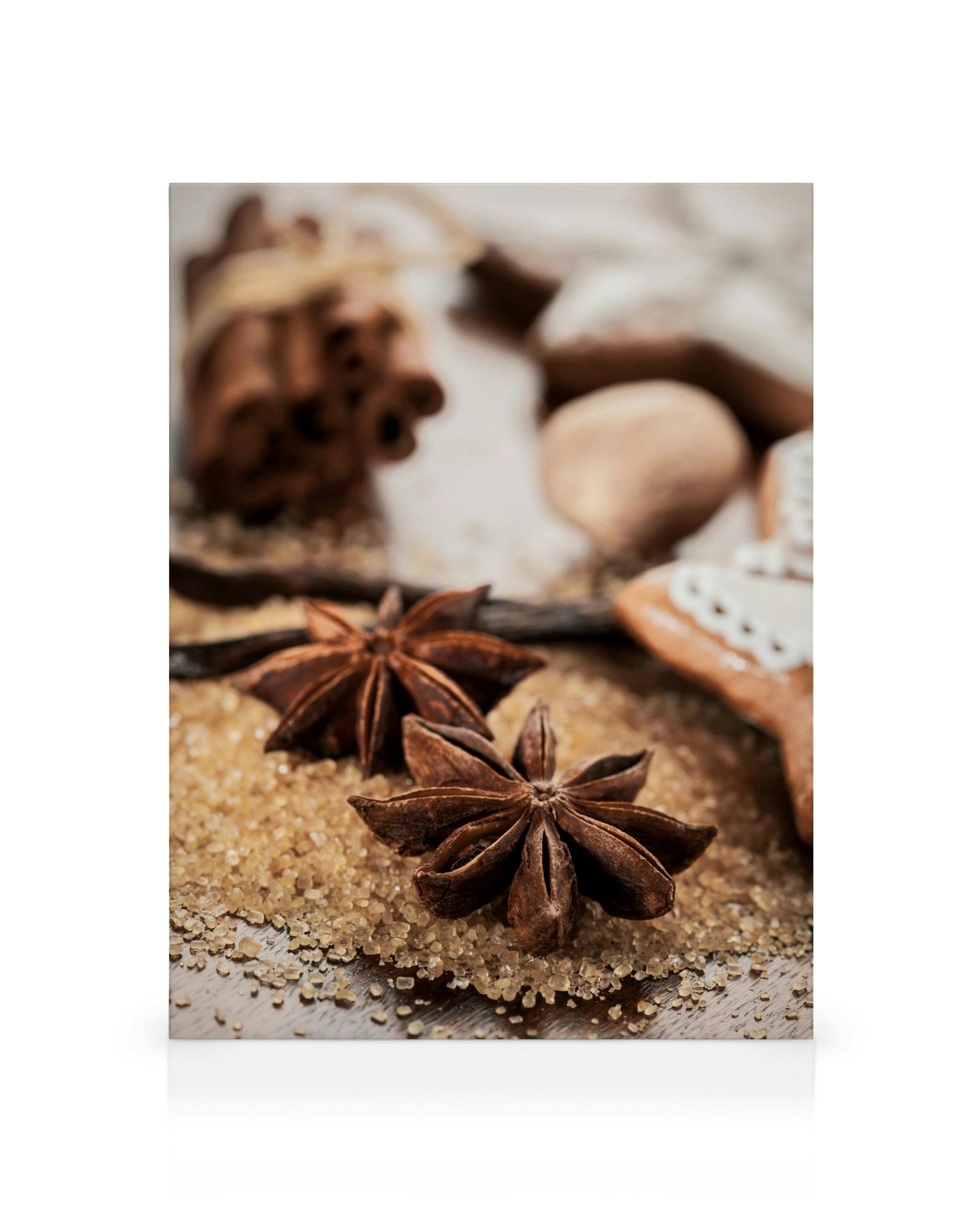 Anise and cinnamon sticks on a bed of brown sugar, with a subtle gingerbread cookie and vanilla bean in the background.