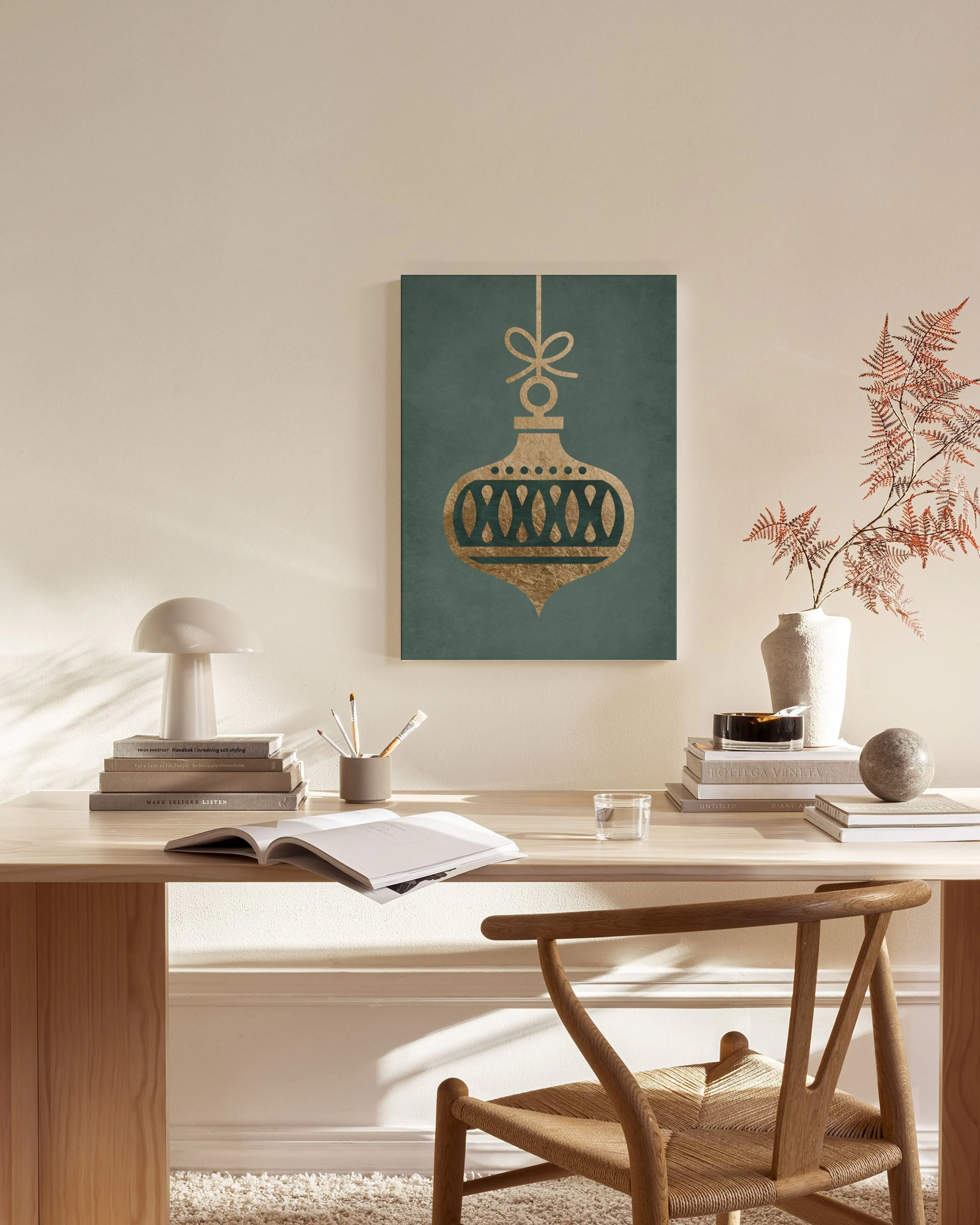 A gold Christmas ornament with a bow on a dark teal background, hanging in a minimalist living room.