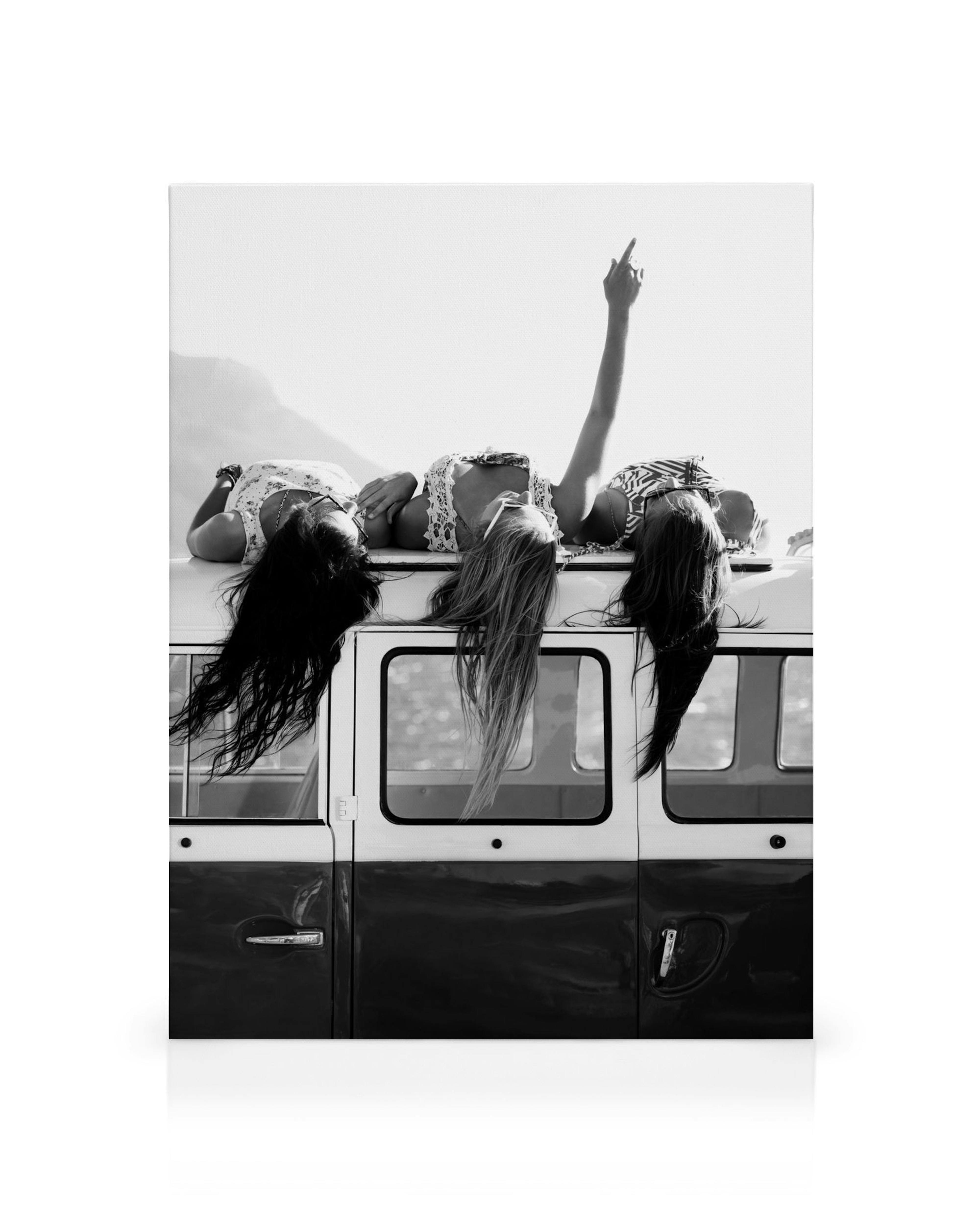 Schwarz-weißes Leinwandbild mit drei Frauen auf dem Dach eines Vans, die Haare wehen im Wind, eine Hand zeigt zum Himmel.