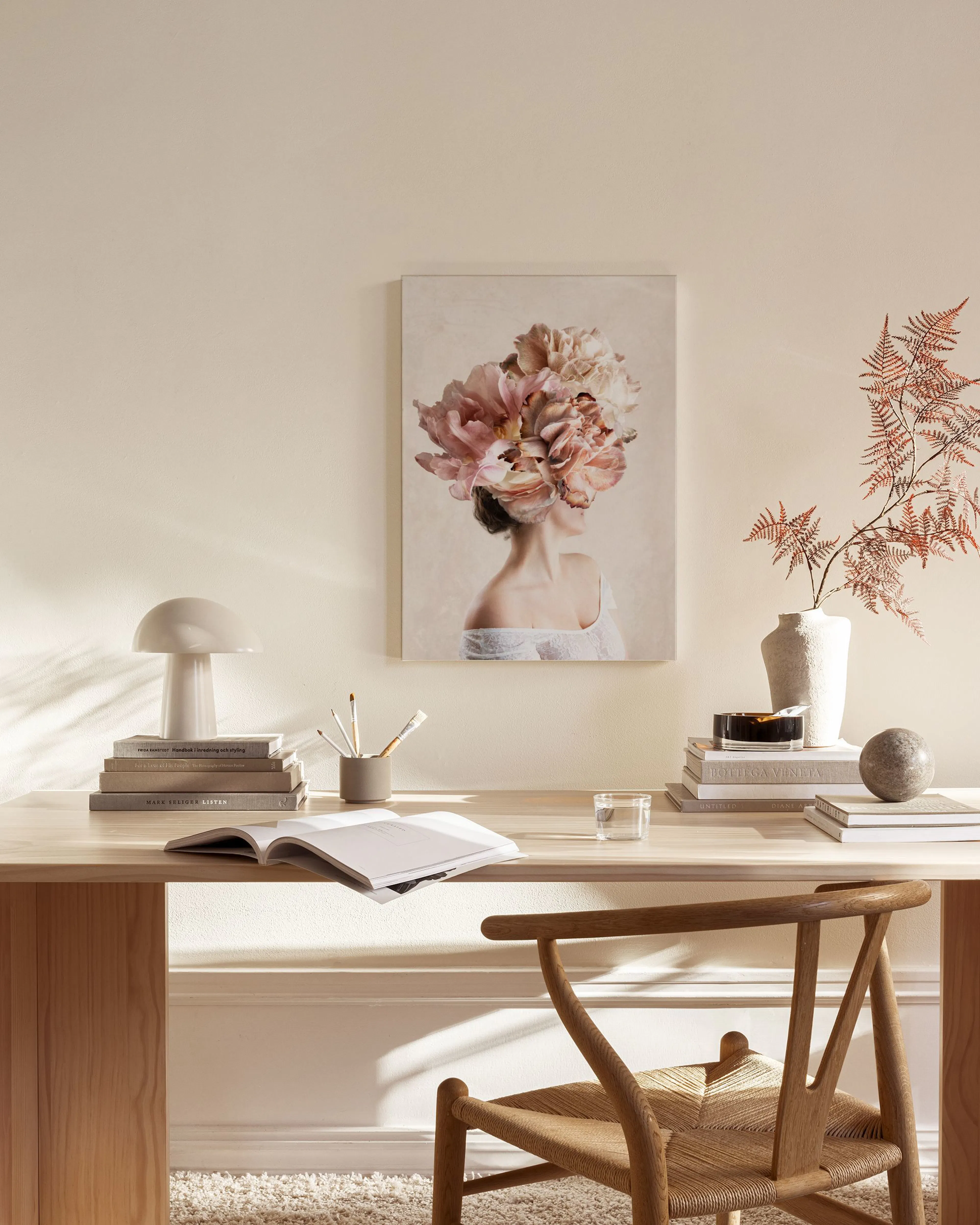 Lerretsbilde av en kvinne med en overflod av rosa og beige blomster som hår, henger i en moderne stue over en benk.