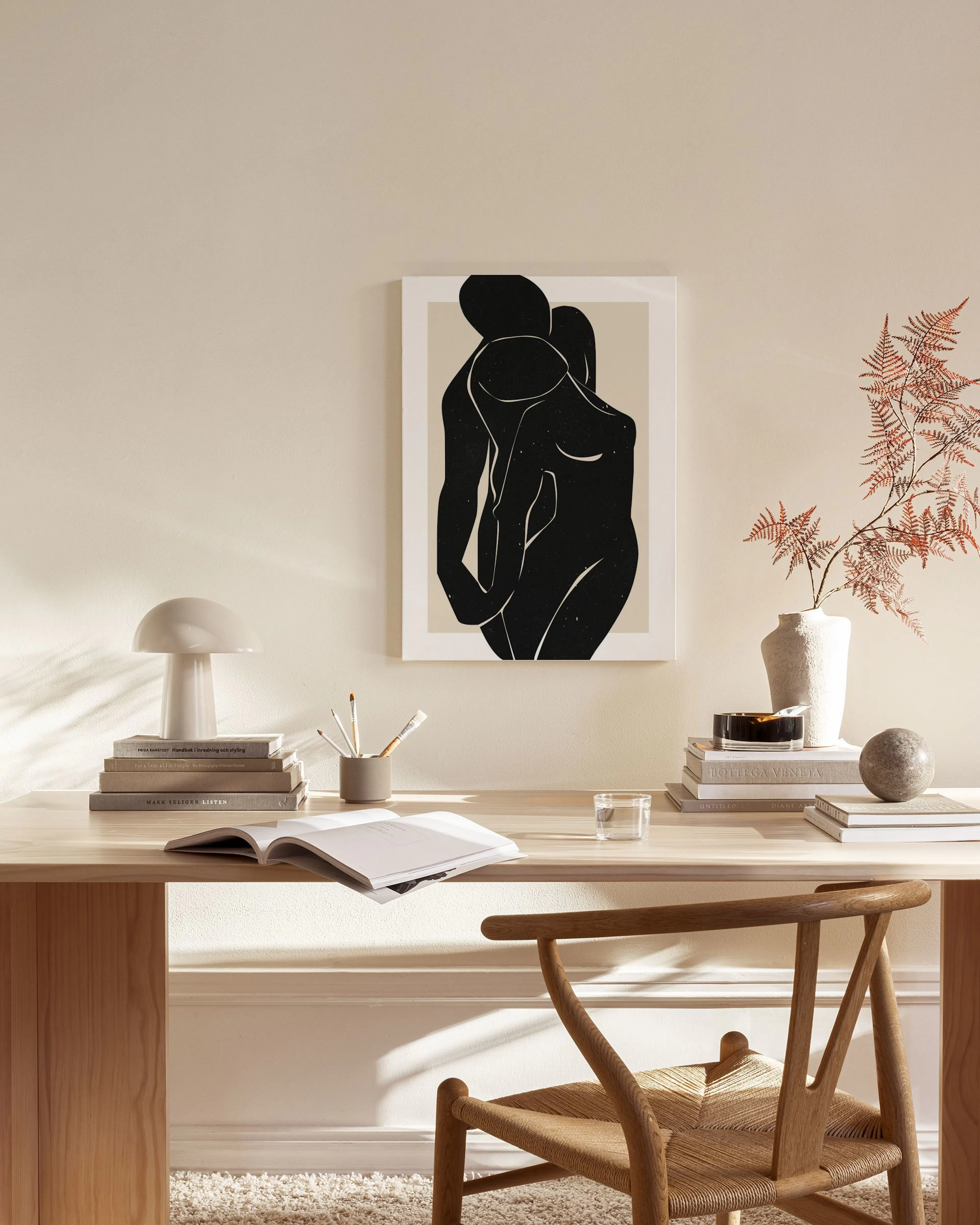 Minimalist black abstract figures embracing on a beige background, hanging in a modern, neutral-toned living room.