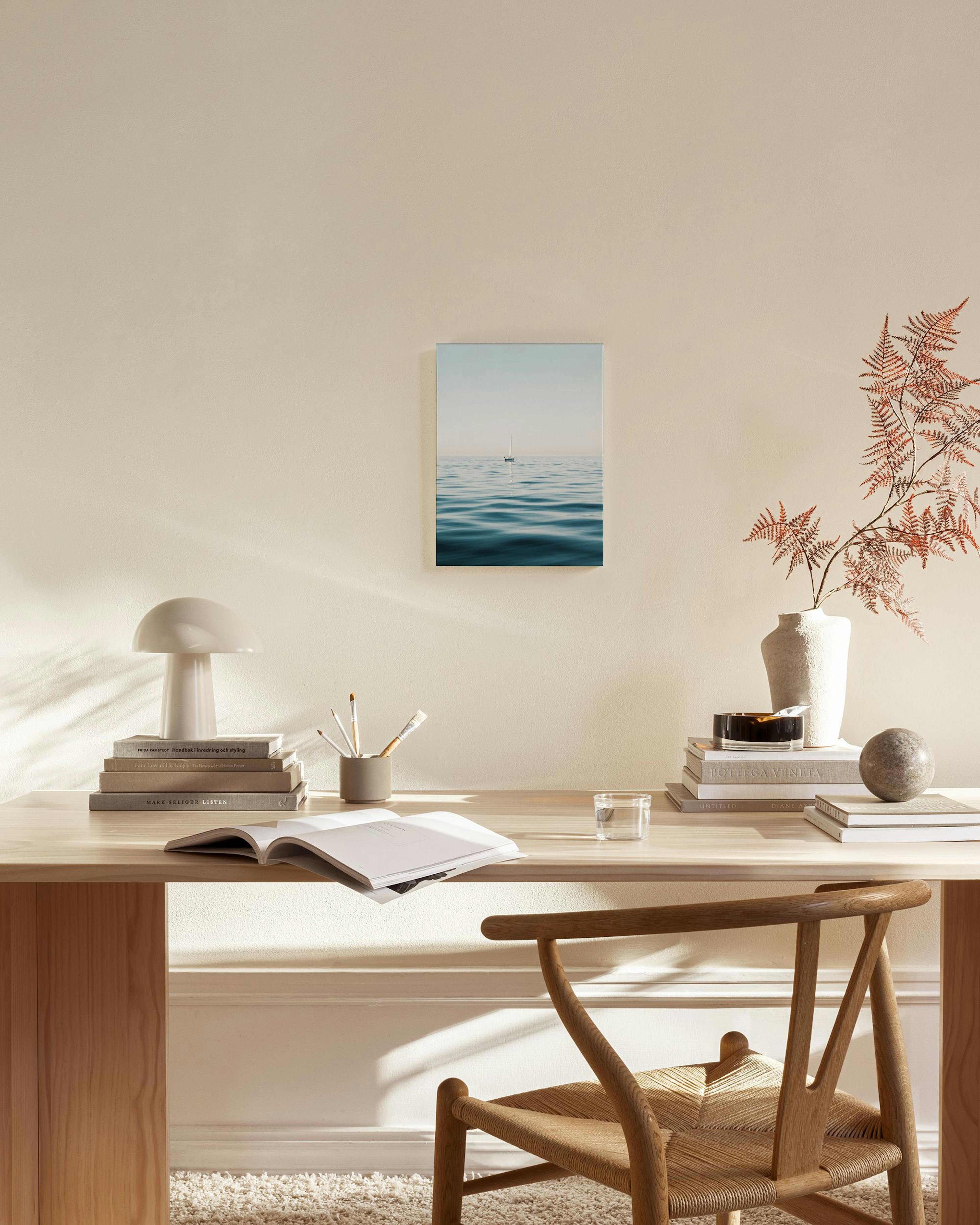 A minimalist canvas print of a distant sailboat on calm blue ocean waves, hanging in a bright, modern living room.