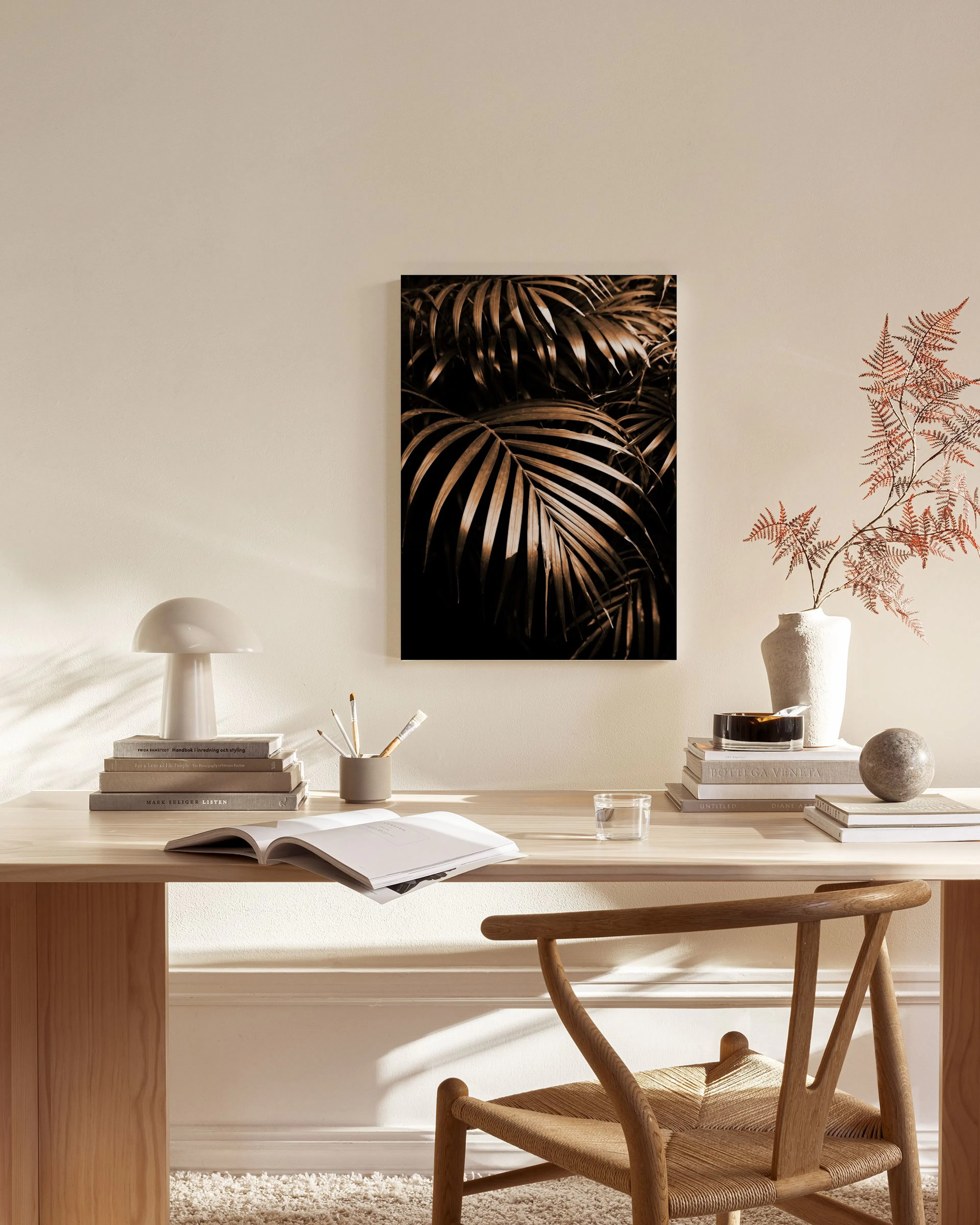 A canvas print of golden palm leaves on a dark background, hanging in a bright, modern living room.