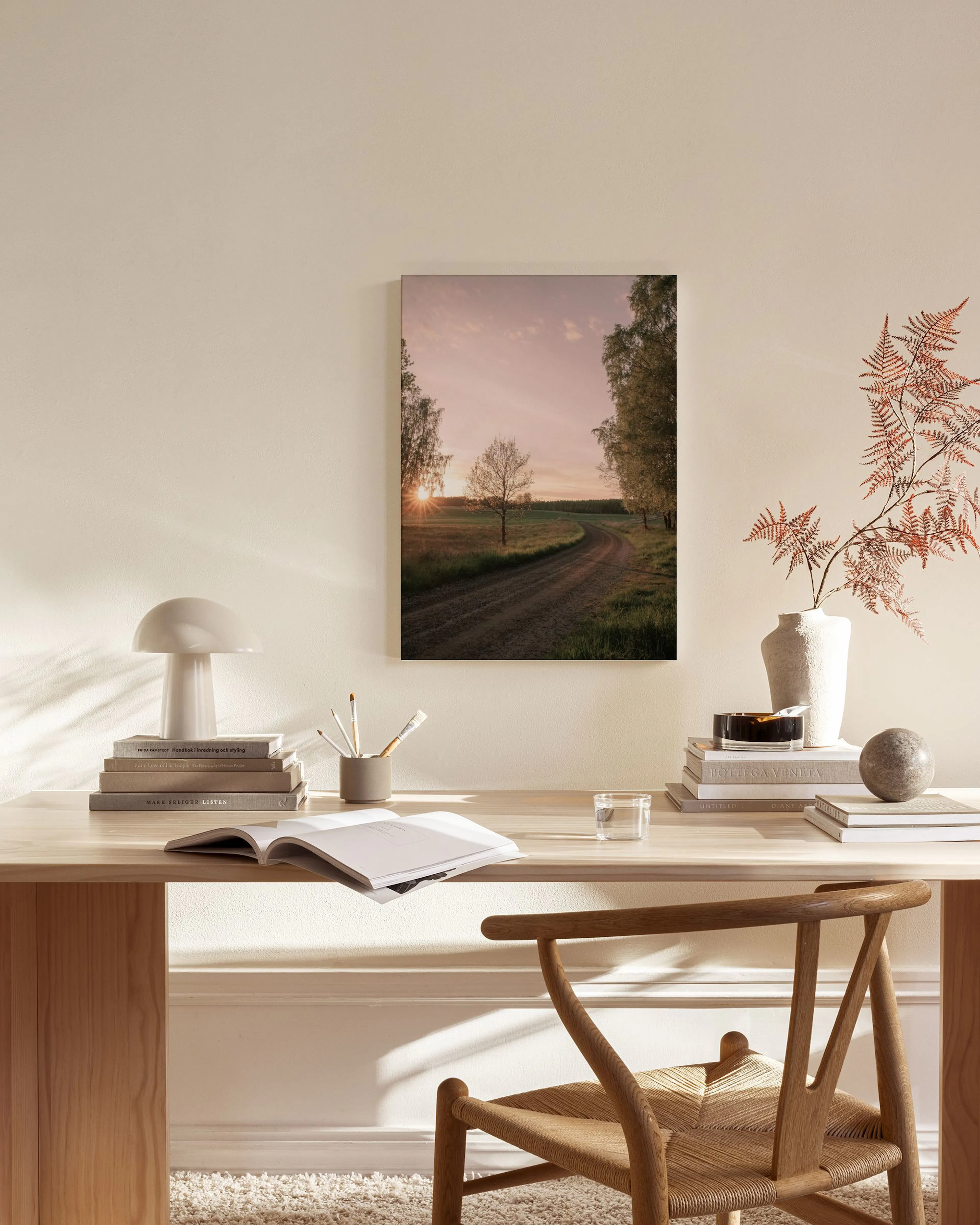 A canvas print of a dirt road winding through fields with trees at sunset, hanging in a minimalist living room.