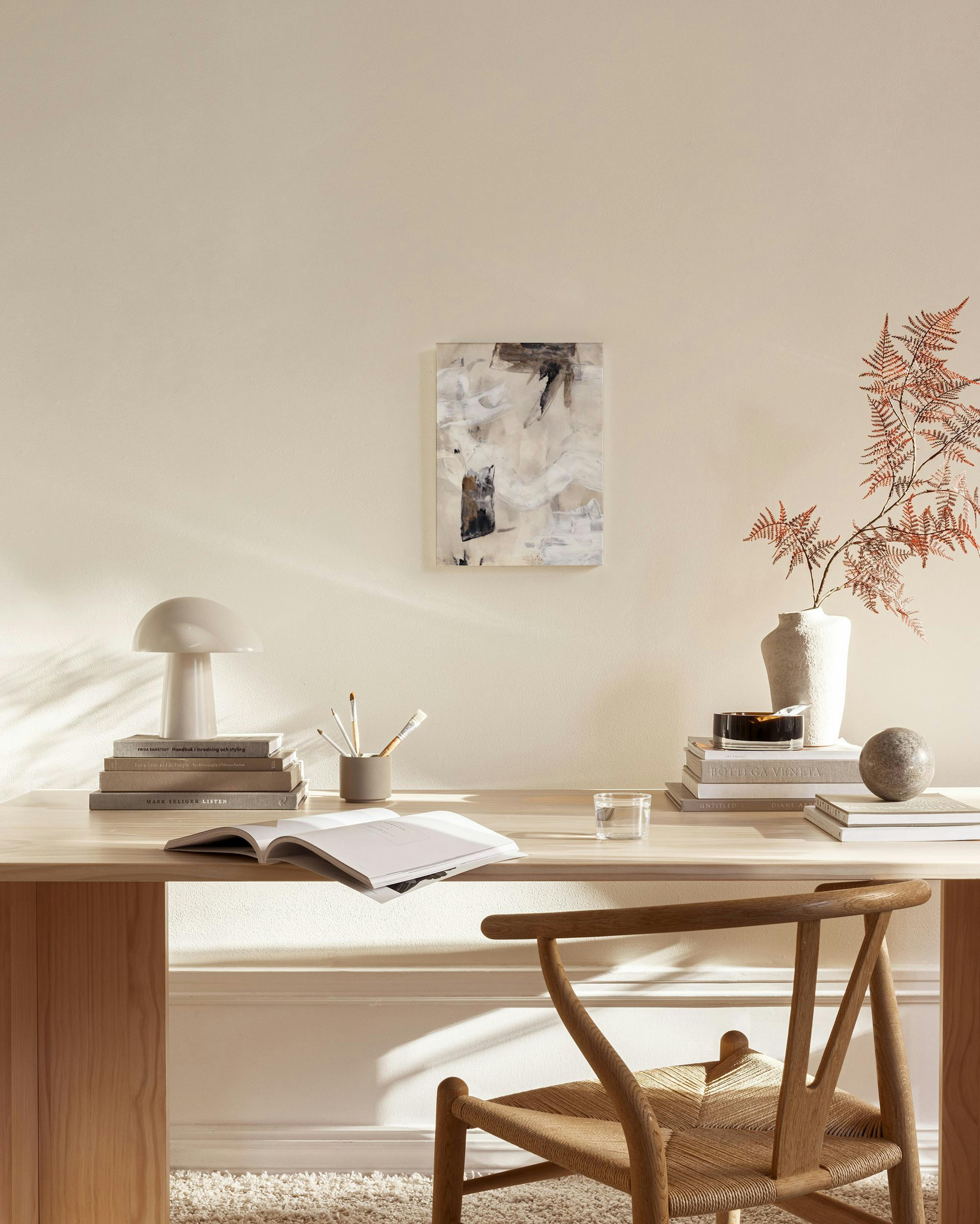 Toile abstraite aux formes beige, marron foncé et blanches, suspendue au-dessus dun banc en bois dans un salon moderne.