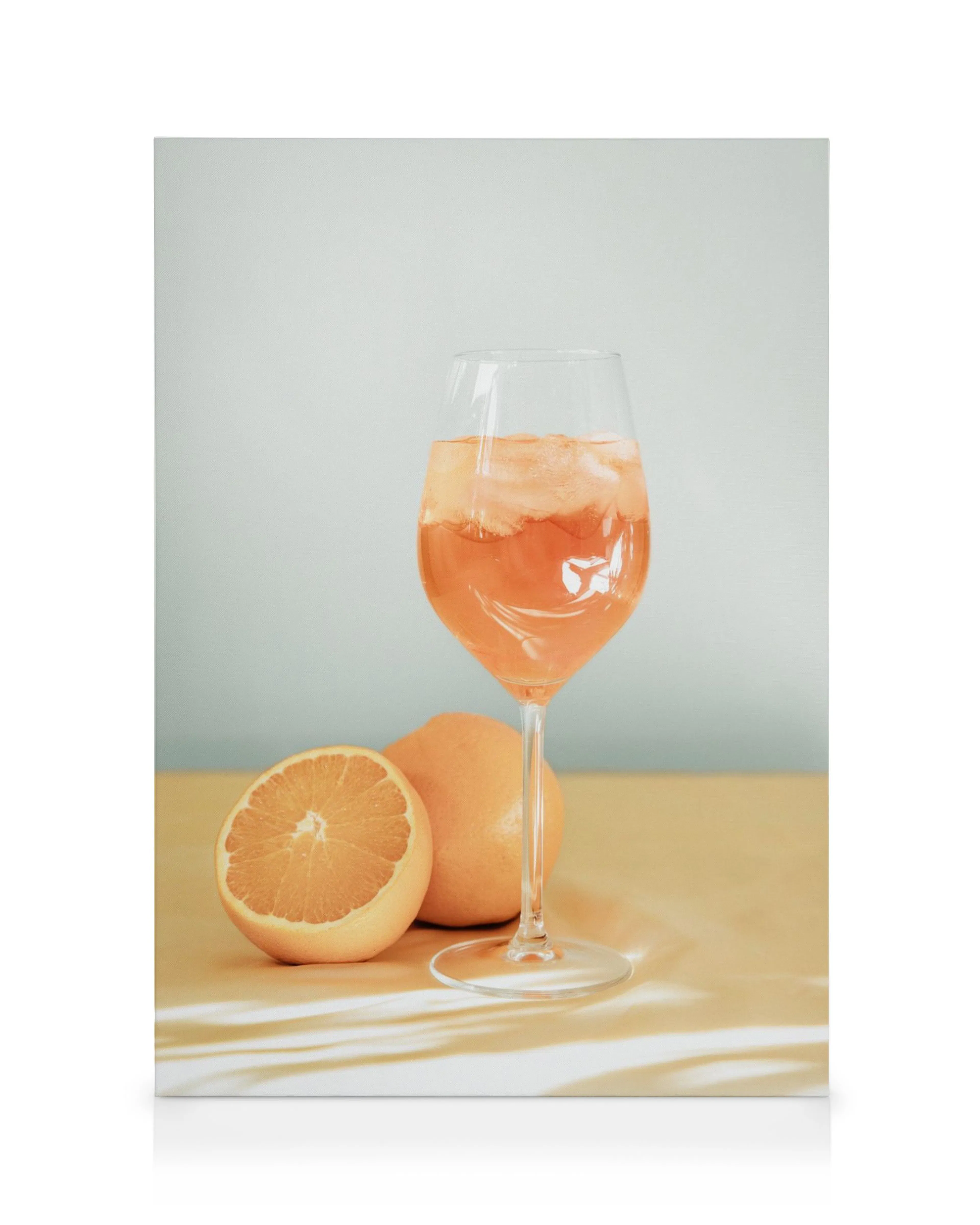 Aperol Spritz drink lærred, et glas med orange drik og isterninger, med grapefrugter på et bord.