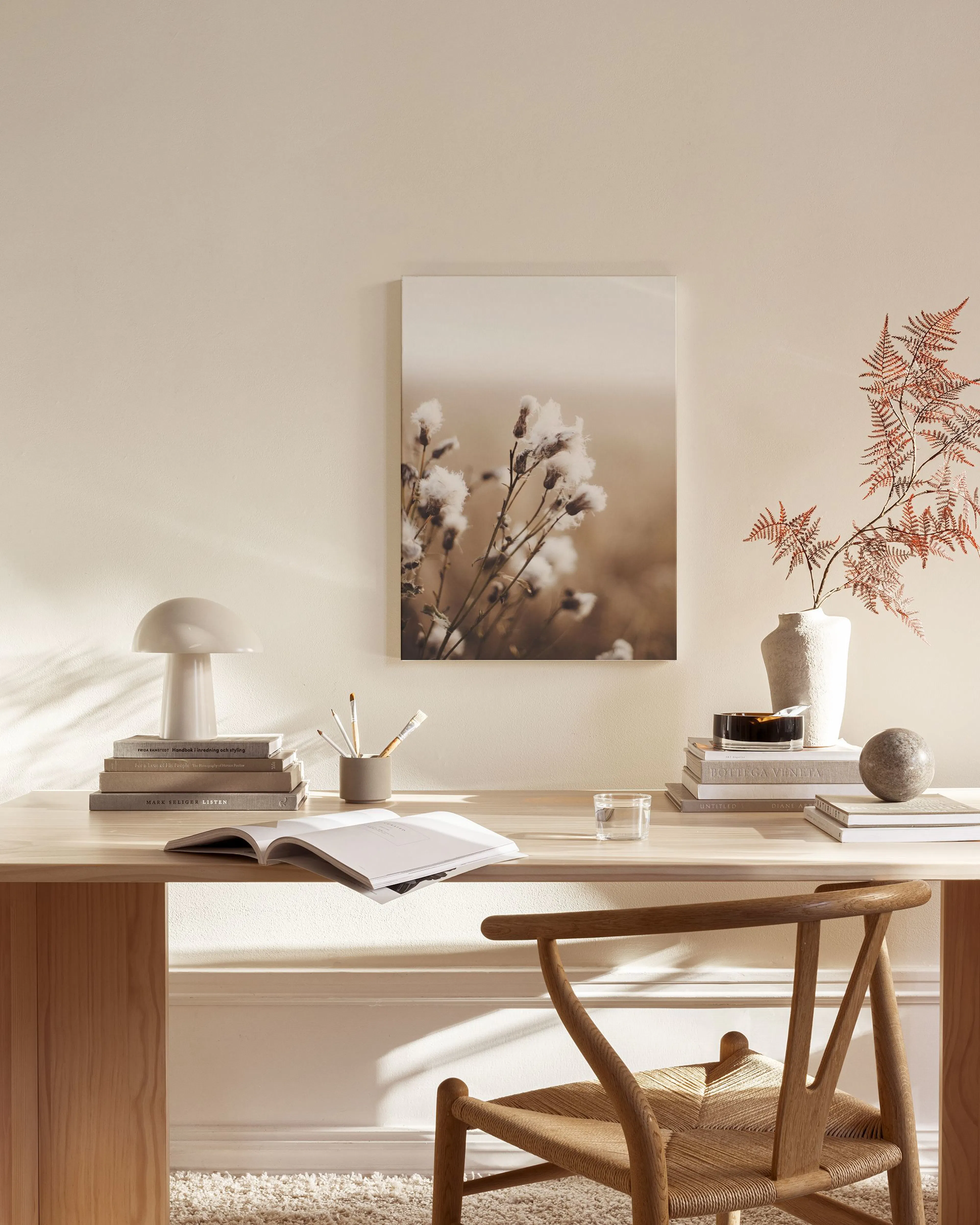 Lerretsbilde av tistelblomster i jordfarger, henger over en benk i et lyst, moderne rom.