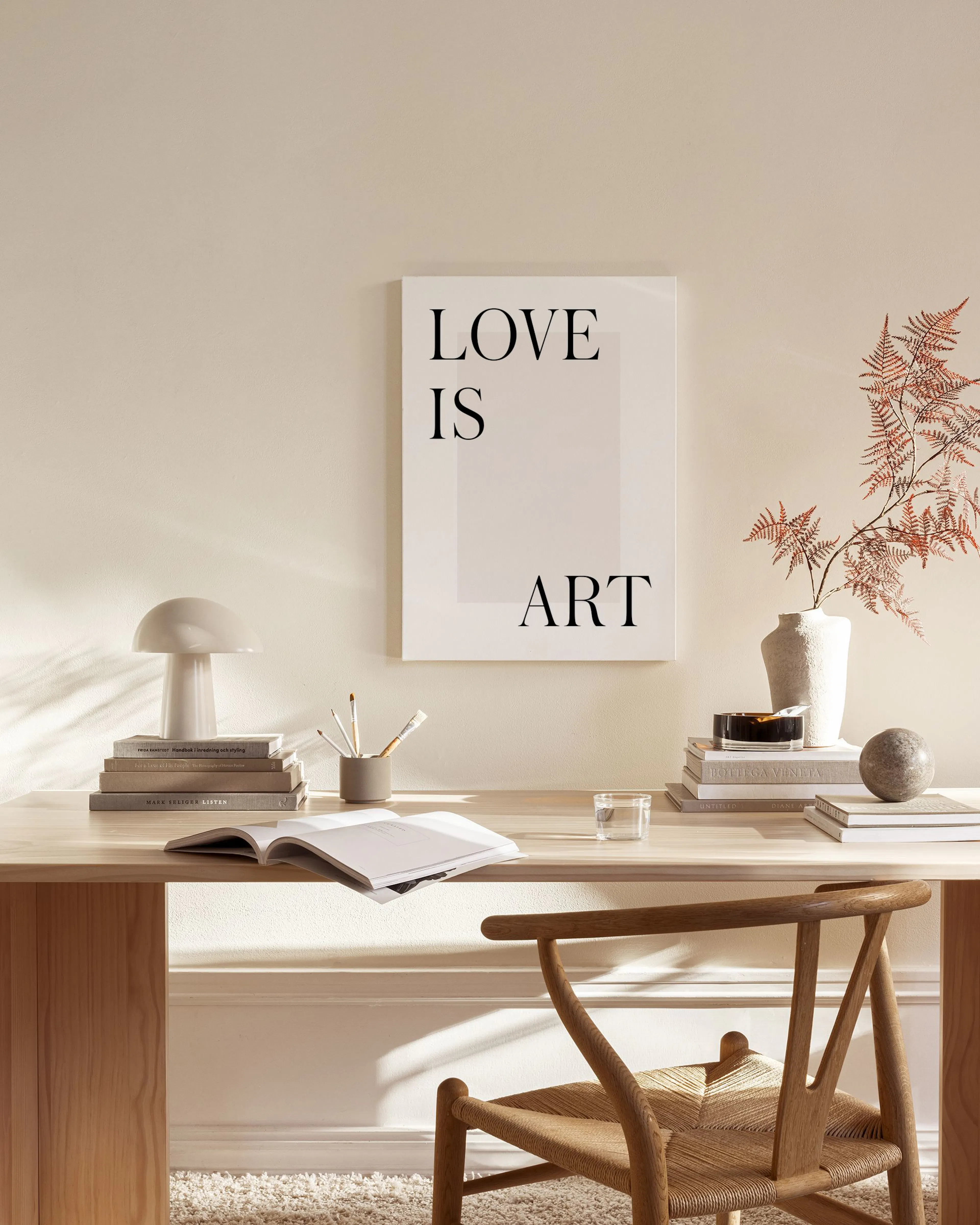 A canvas print with the text LOVE IS ART hanging in a minimalist living room above a wooden console.