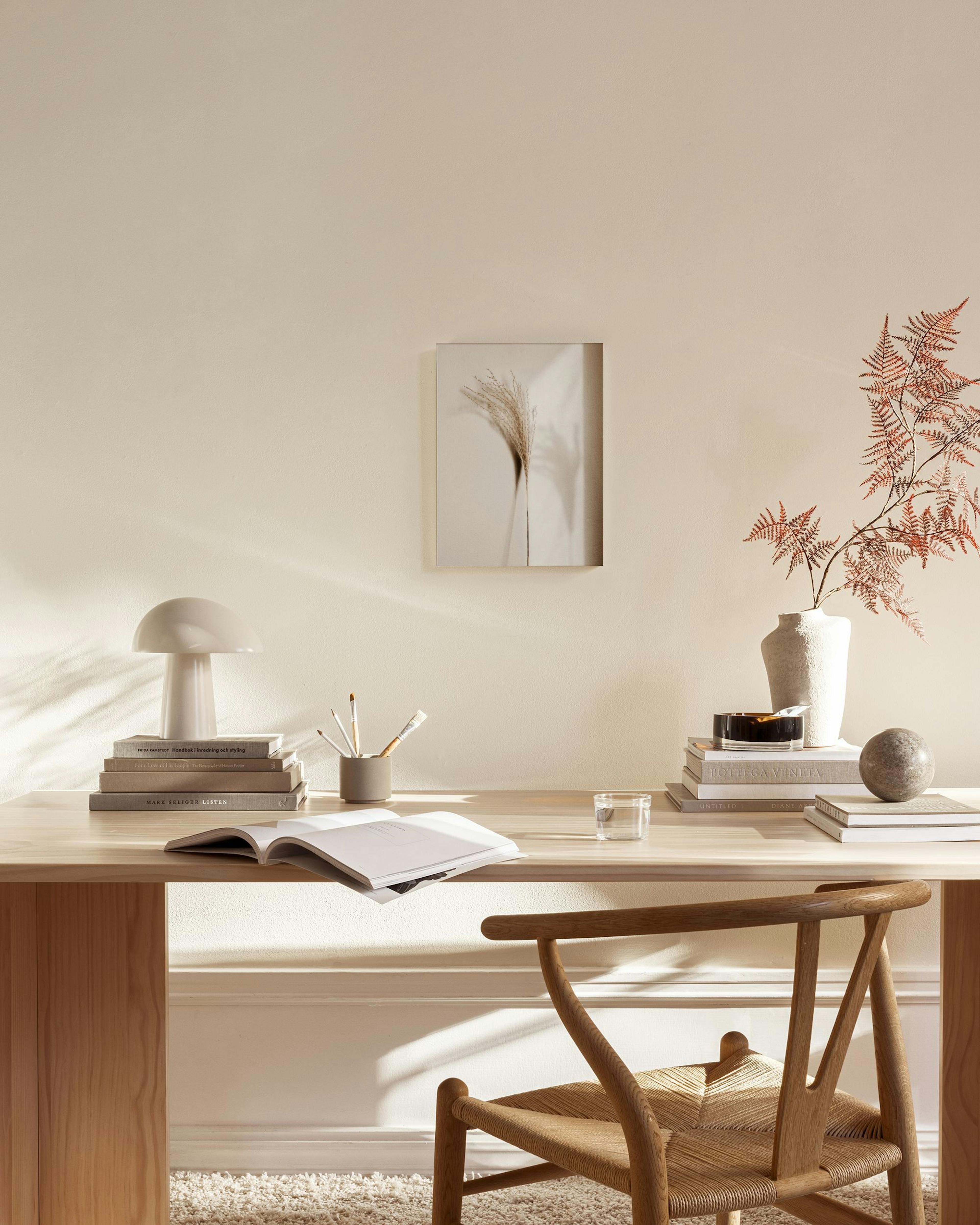 A minimalist print of dried pampas grass with a shadow, hanging in a neutral-toned living room above wooden furniture.