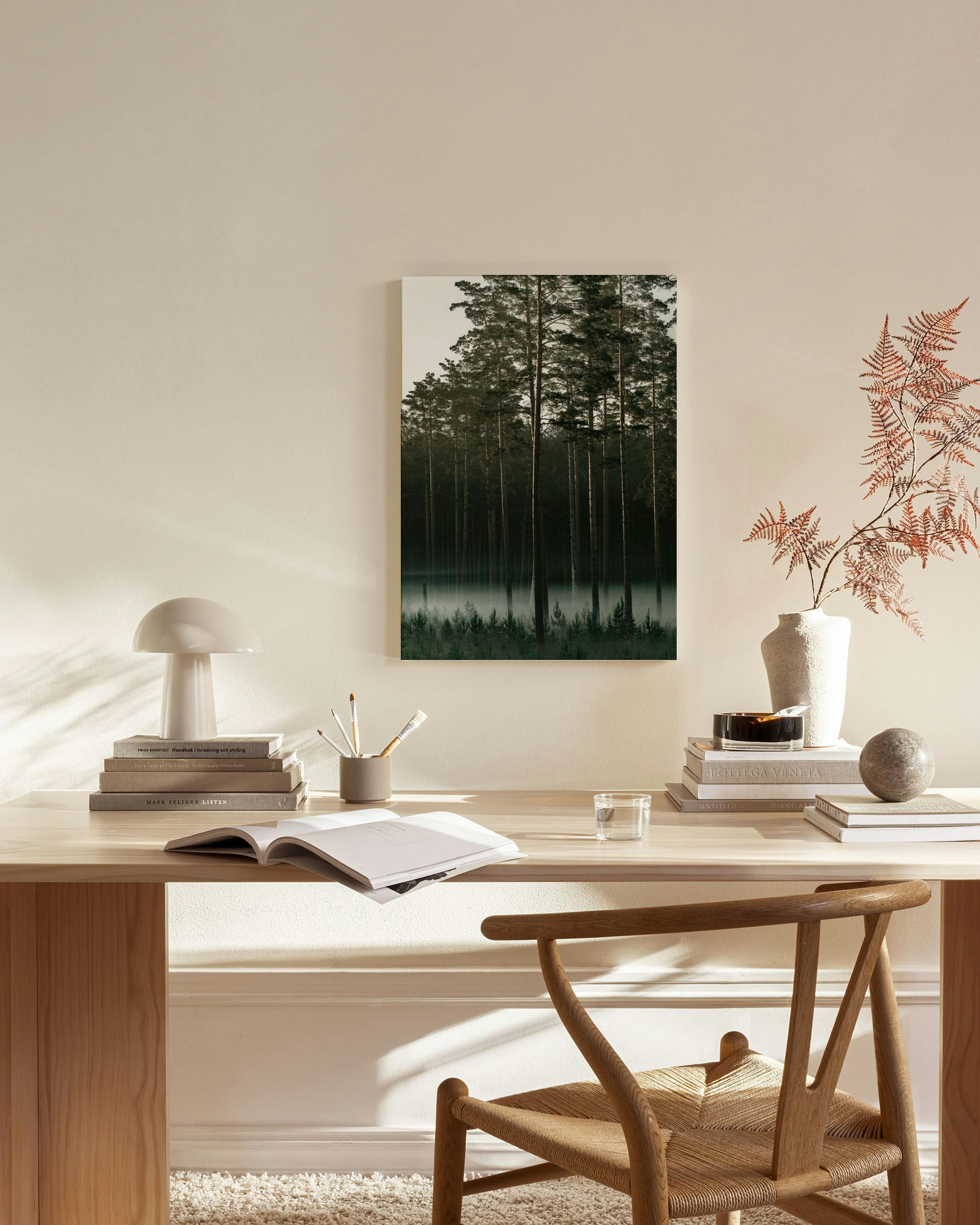Lærred med et mystisk skovlandskab med træer og dis over vandet, hængende i en stue med en lænestol.