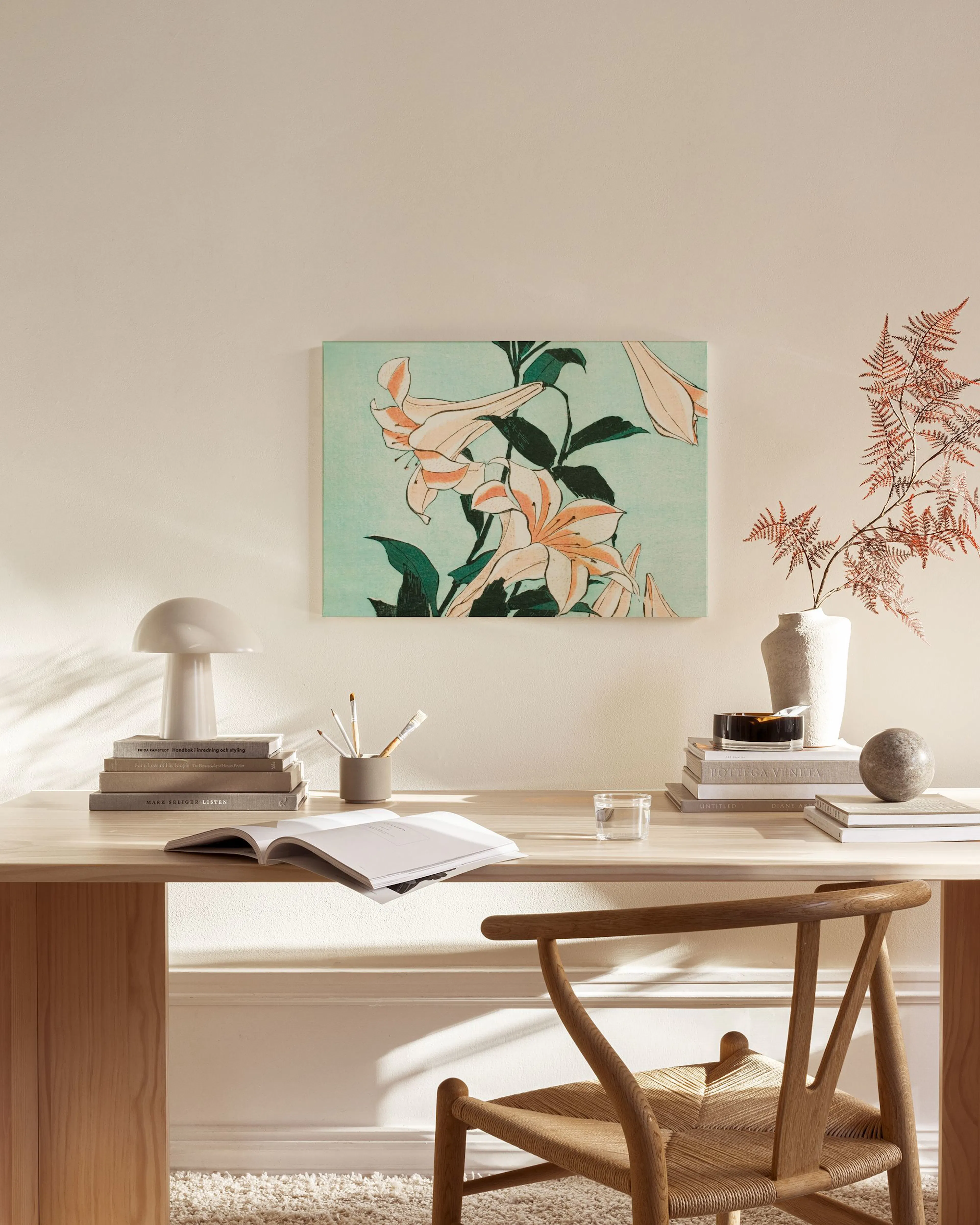 Canvas print of delicate white and peach lilies with green foliage on a light blue background, hanging in a minimalist living ro