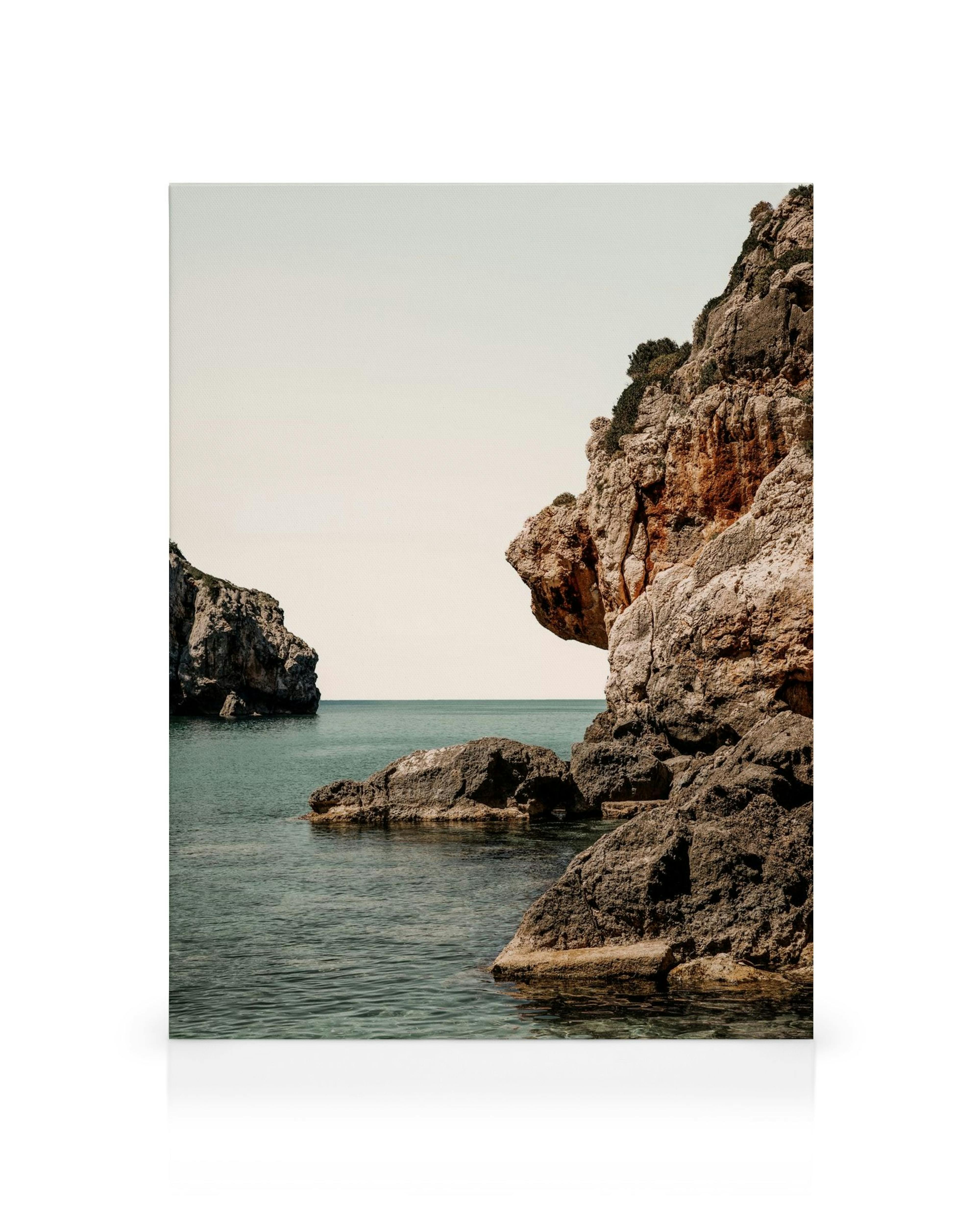 Stampa su tela Endless Summer: rocce frastagliate arancioni e marroni con vegetazione verde, che si estendono su un mare blu cal