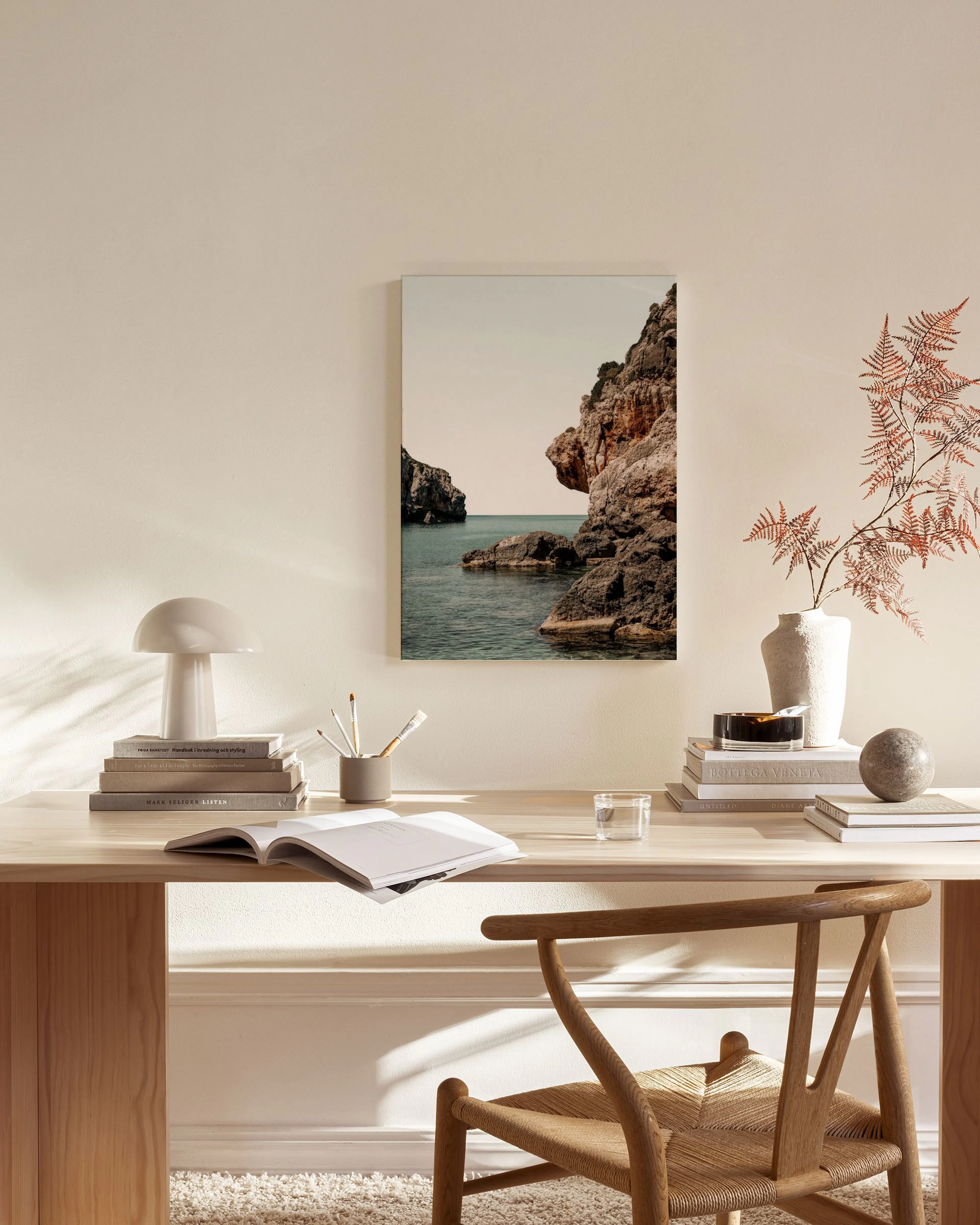 Lienzo de un paisaje marino con rocas escarpadas y agua azul, colgado en una sala de estar moderna sobre un mueble de madera.