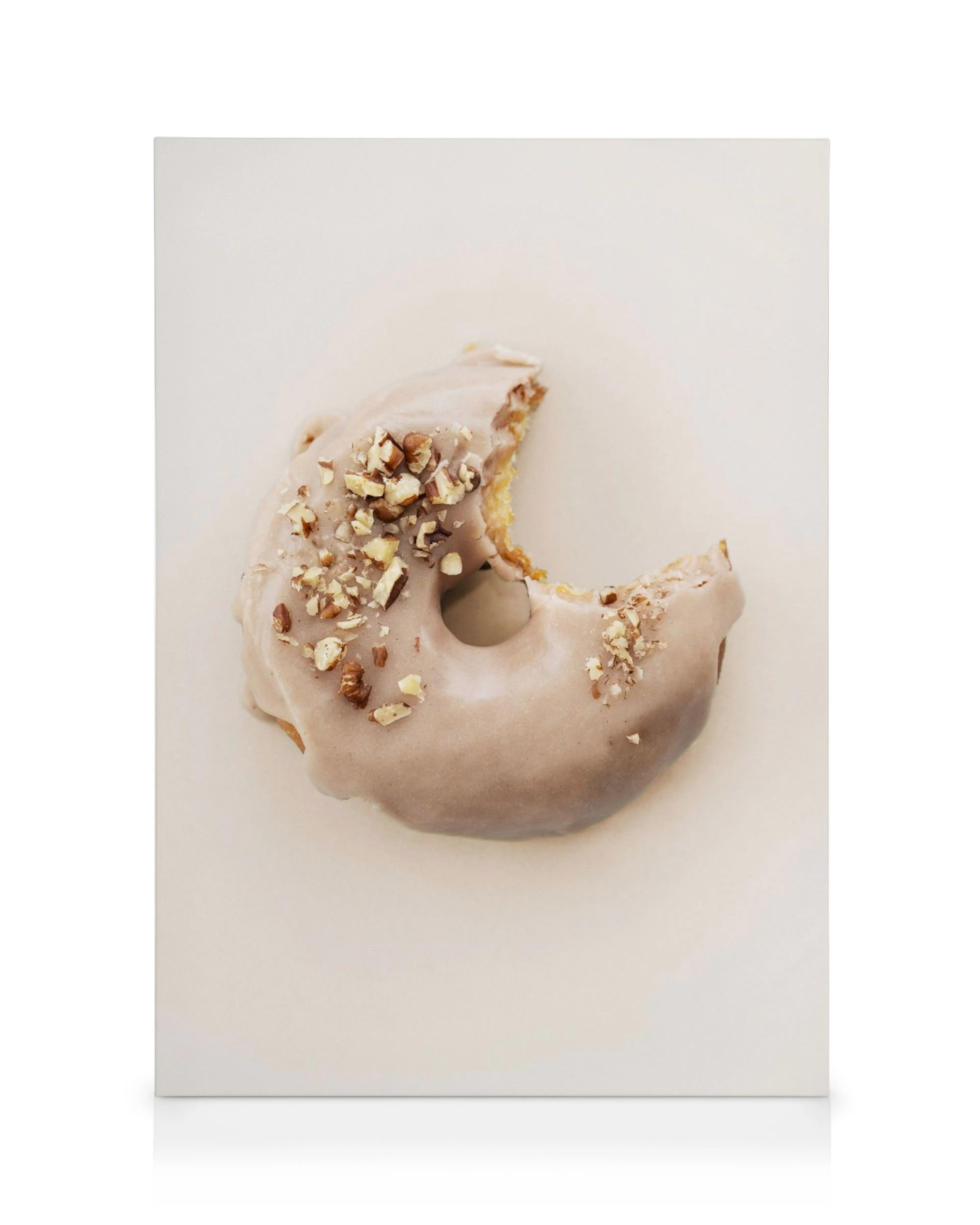 Angebissener Donut mit grauer Glasur und gehackten Nüssen, auf hellem Untergrund. Leckere Donut Kunst Leinwand.