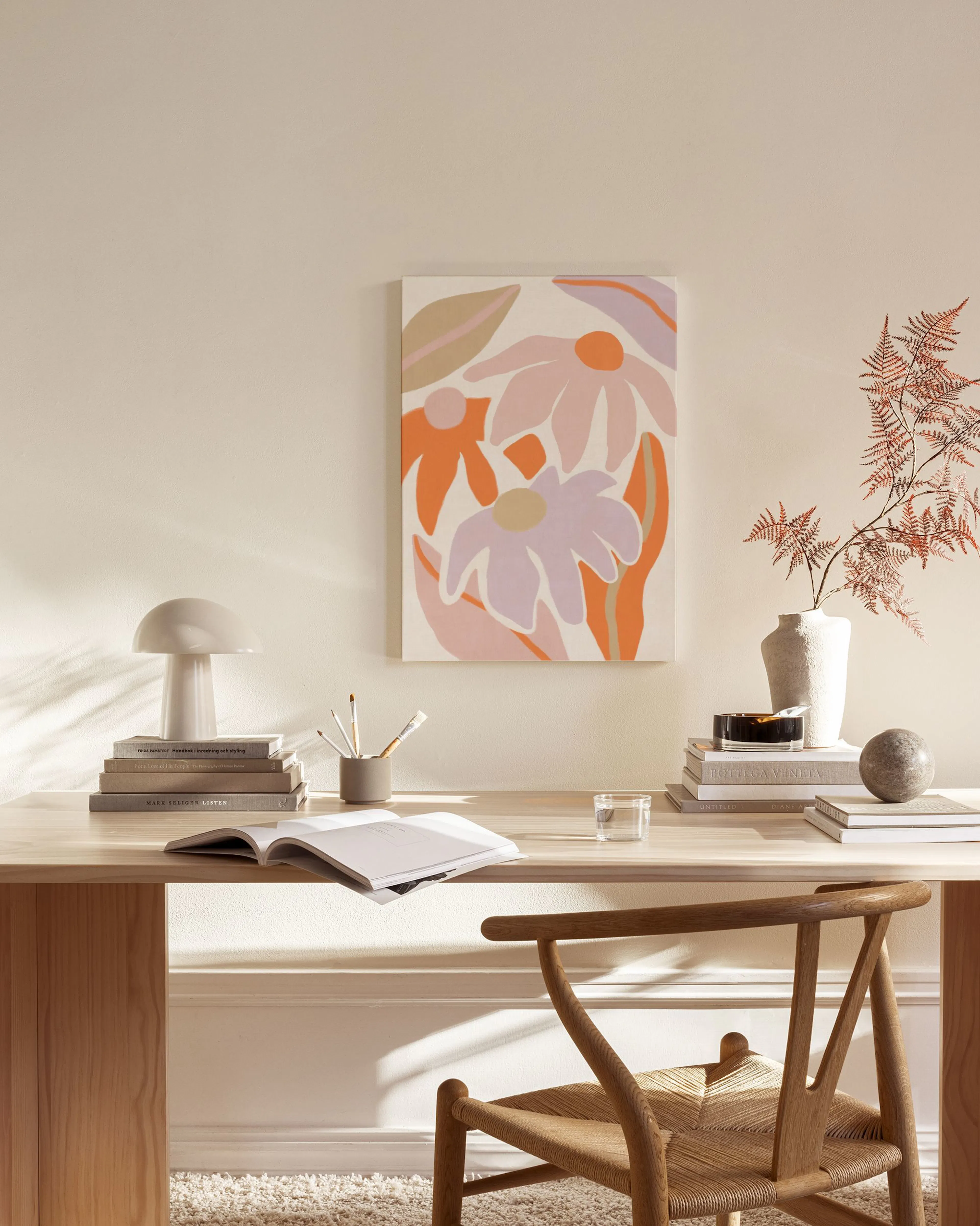 Stampa su tela con fiori astratti in rosa, arancione e lilla, appesa sopra un mobile basso in soggiorno.