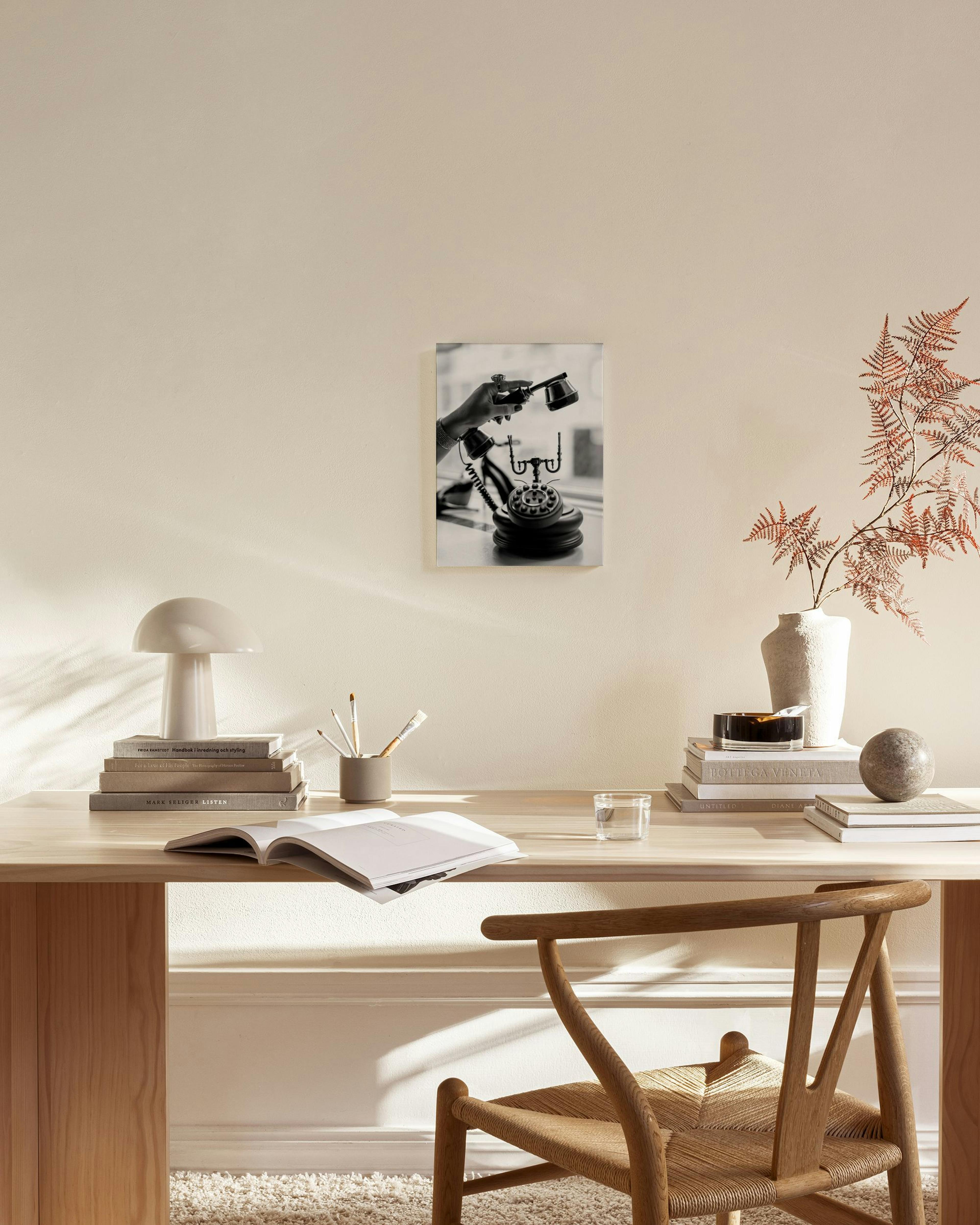 Black and white canvas print of a hand holding a vintage rotary phone, displayed above a wooden console table in a minimalist li