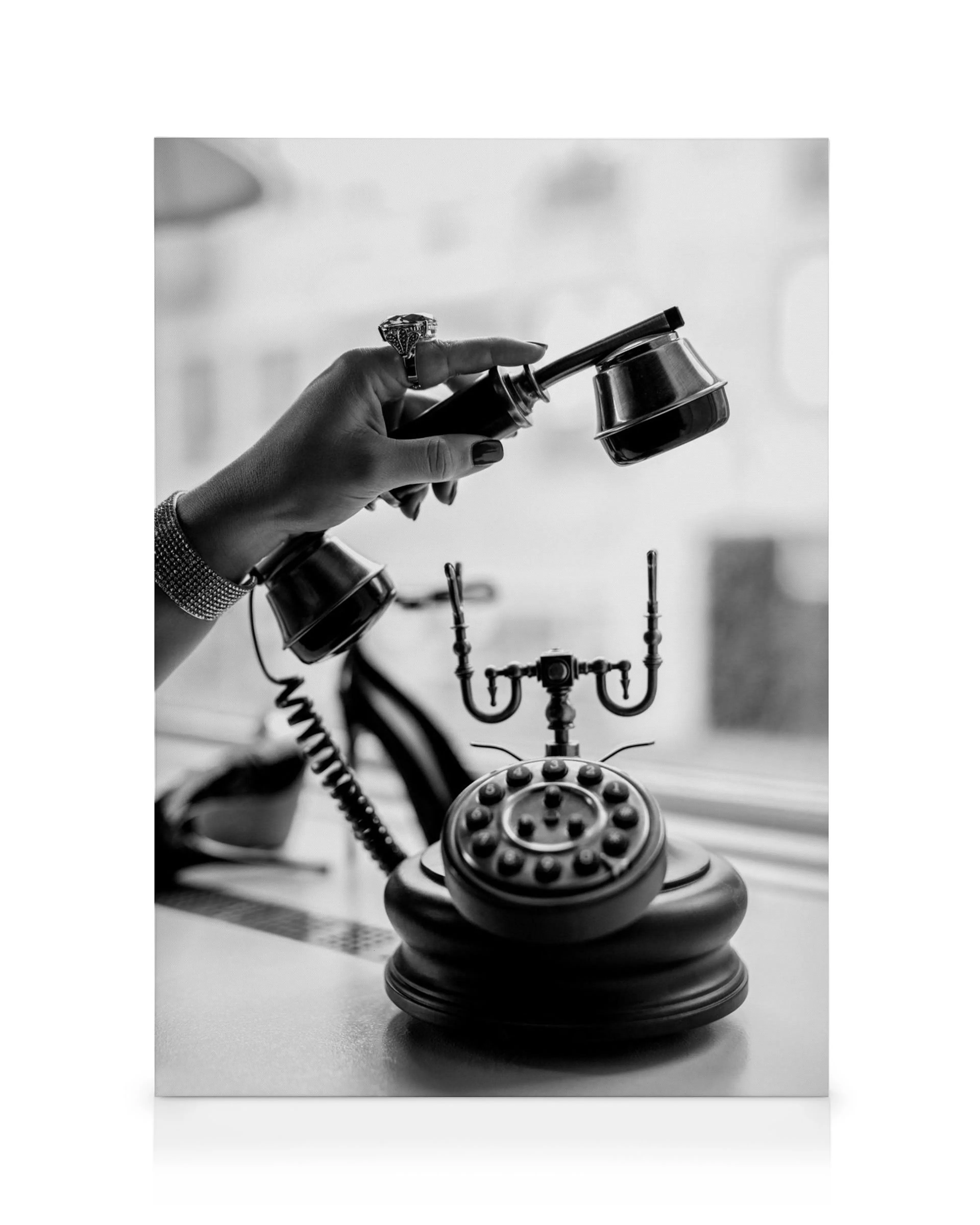Svartvit canvastavla av en hand som håller luren till en vintage telefon med snurrskiva, elegant och retro.