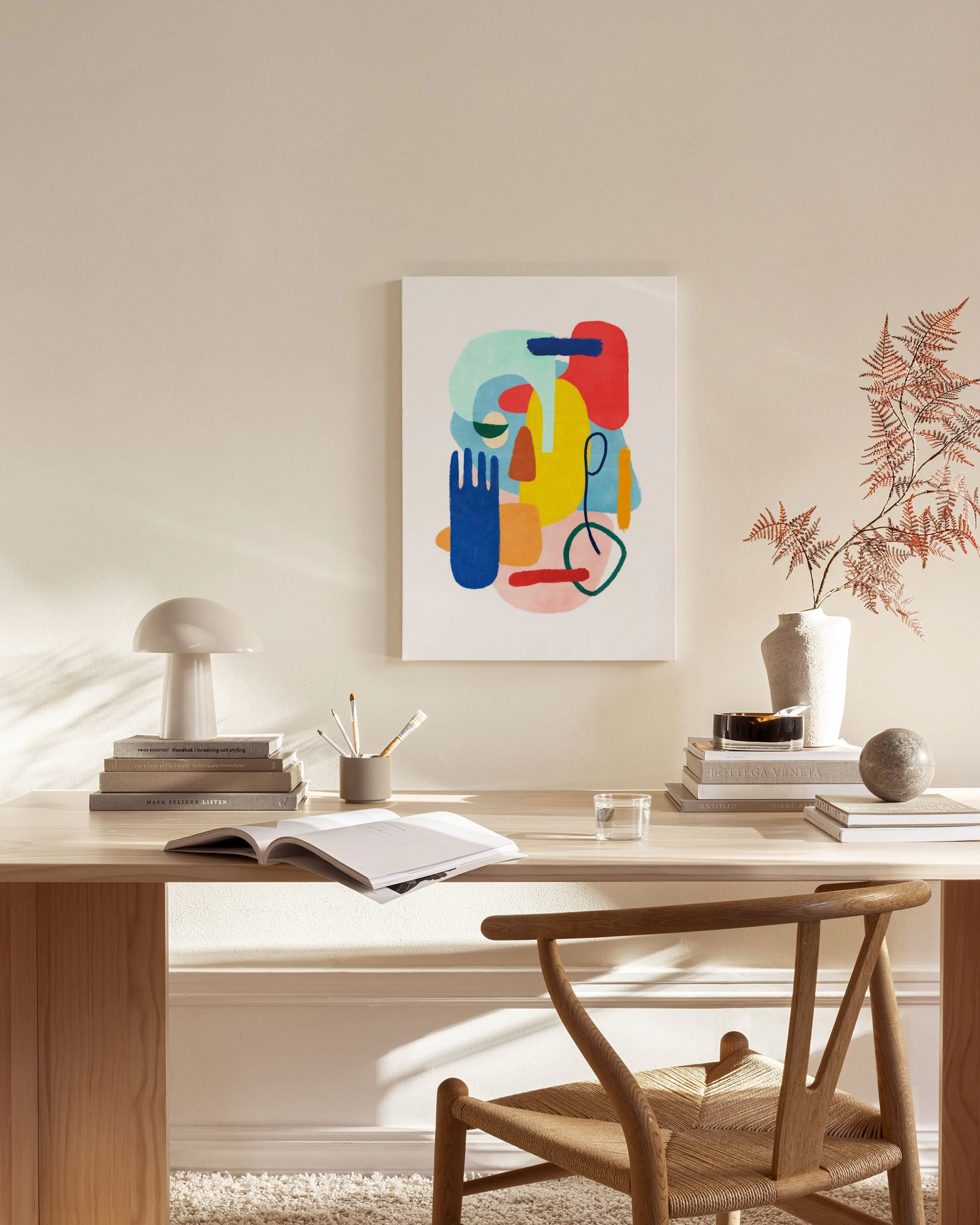 A colourful abstract canvas print with organic shapes in red, blue, yellow, and green, displayed in a modern living room above a