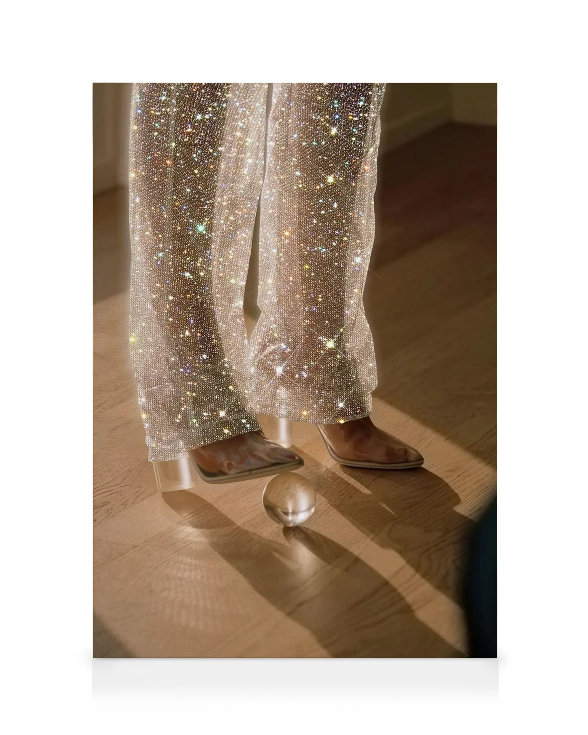 Sparkling silver glitter pants and brown boots on a wooden floor with a glass sphere, reflecting light on this canvas print.