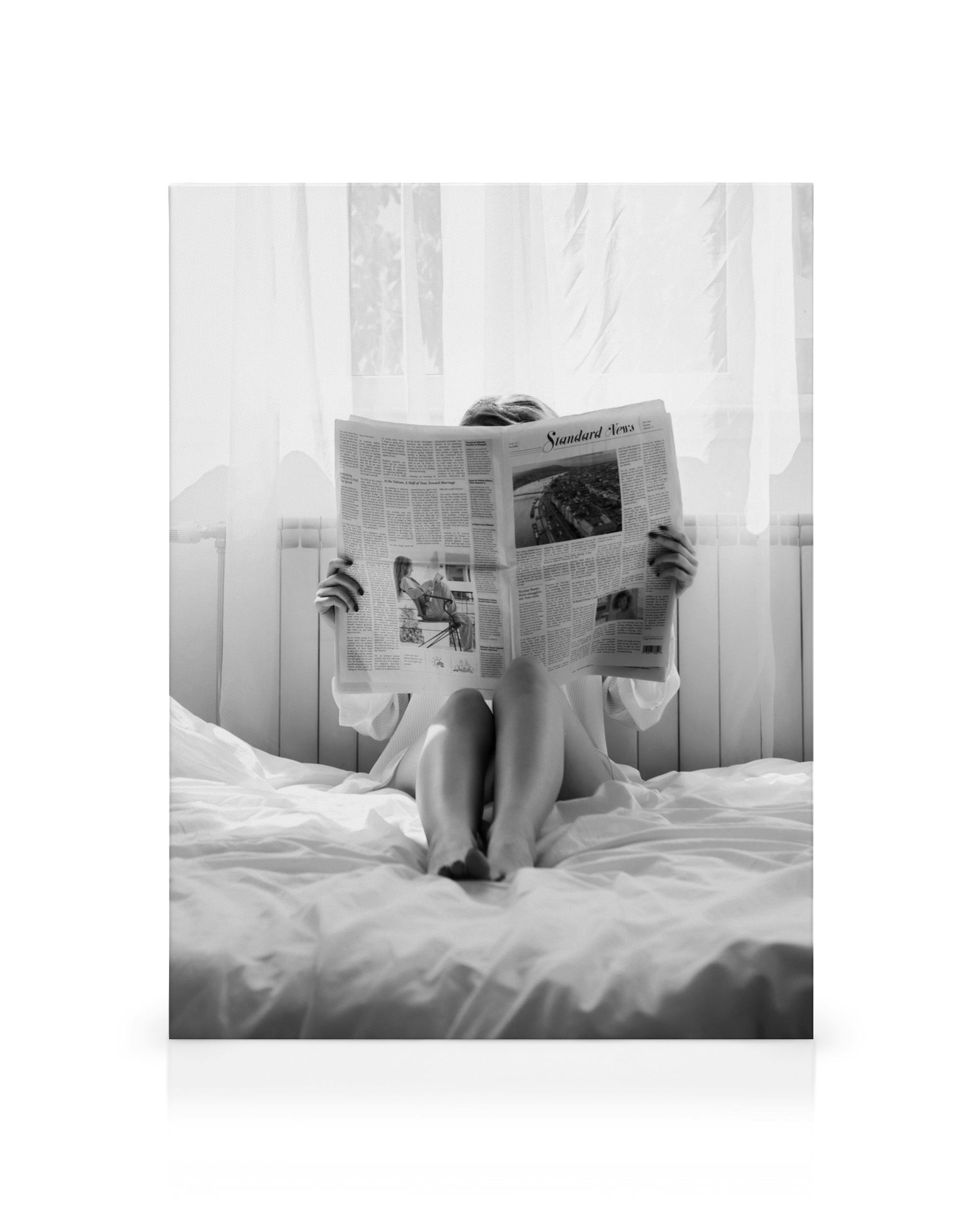 Černobílý obraz ženy v posteli čtoucí noviny, ranní klid