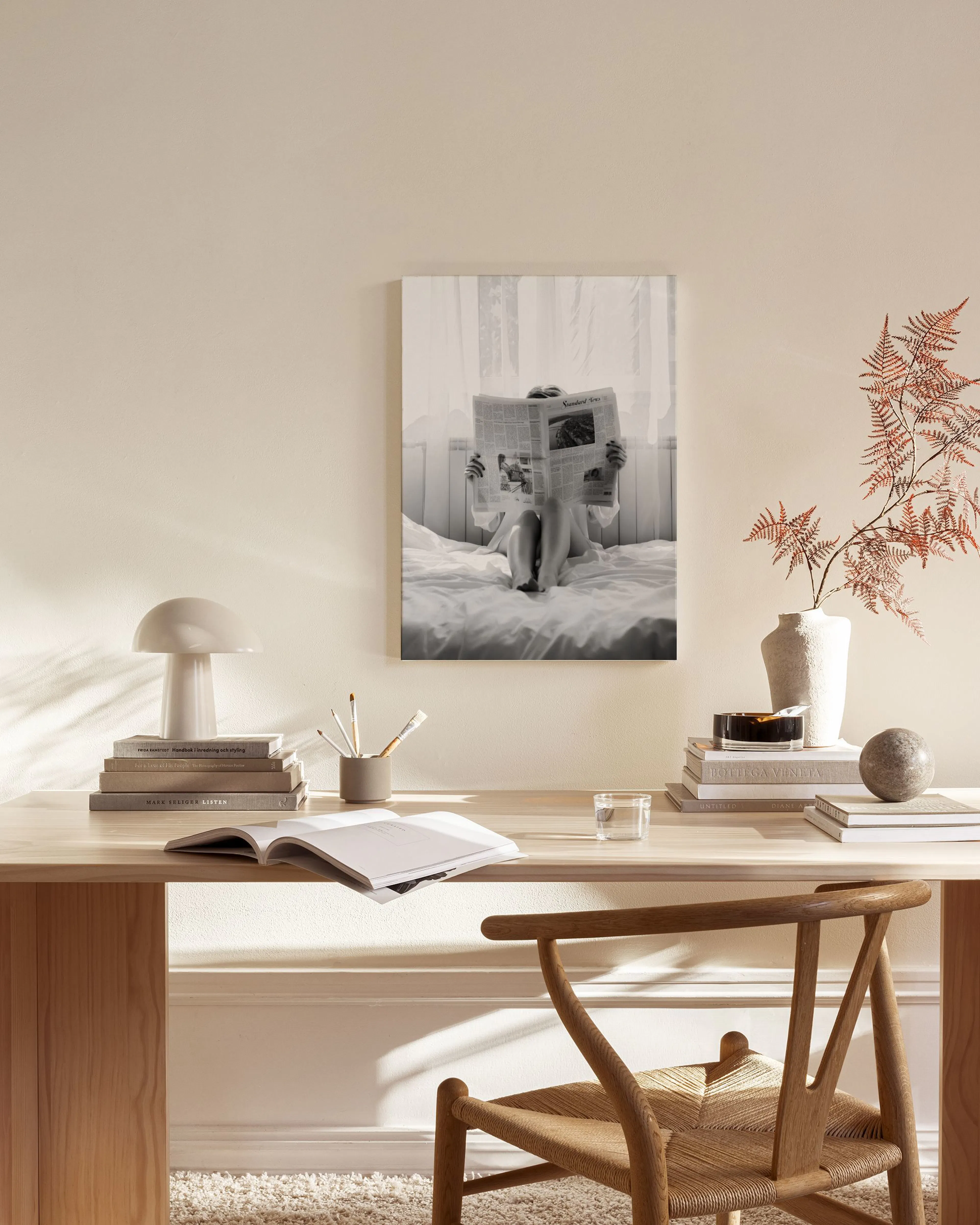 Sort-hvid fotokunst af person, der læser avis i seng, hængende i en stue med lyse møbler.