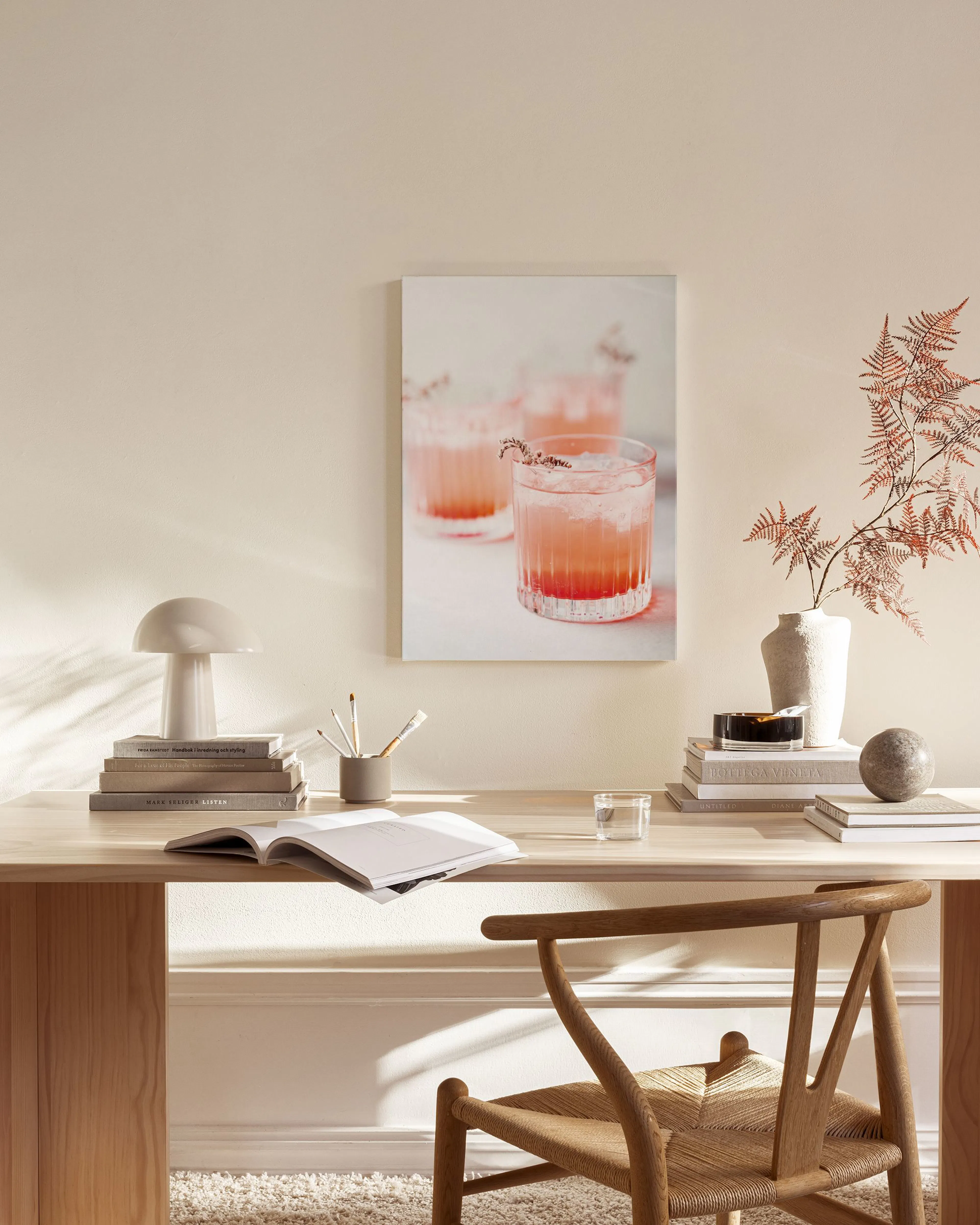 Canvastavla med tre rosa drinkar i glas, hängande i ett ljust vardagsrum över en träbänk.