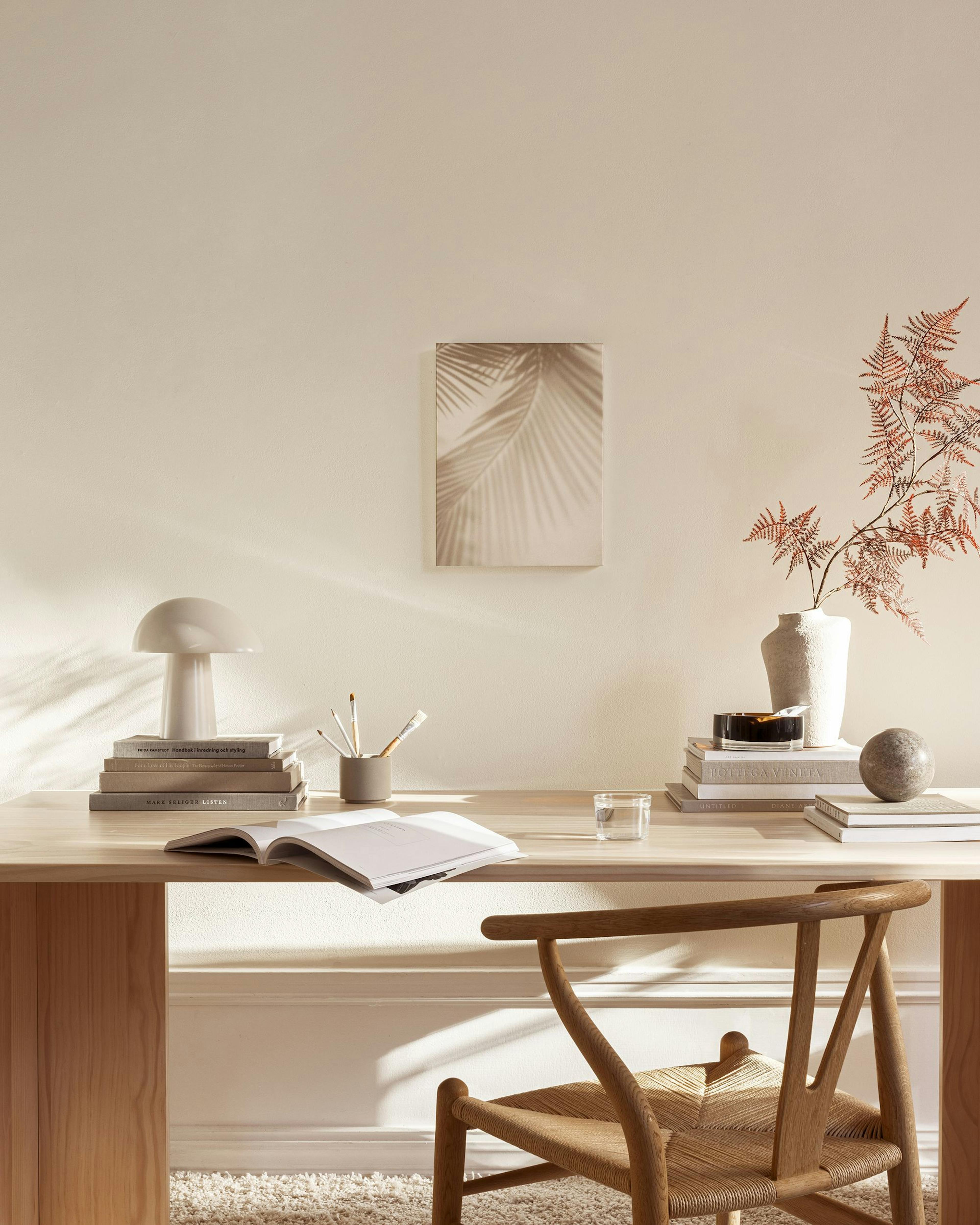 Canvas met beige palmbladeren en schaduwen, hangend in een moderne, minimalistische woonkamer boven een houten dressoir.