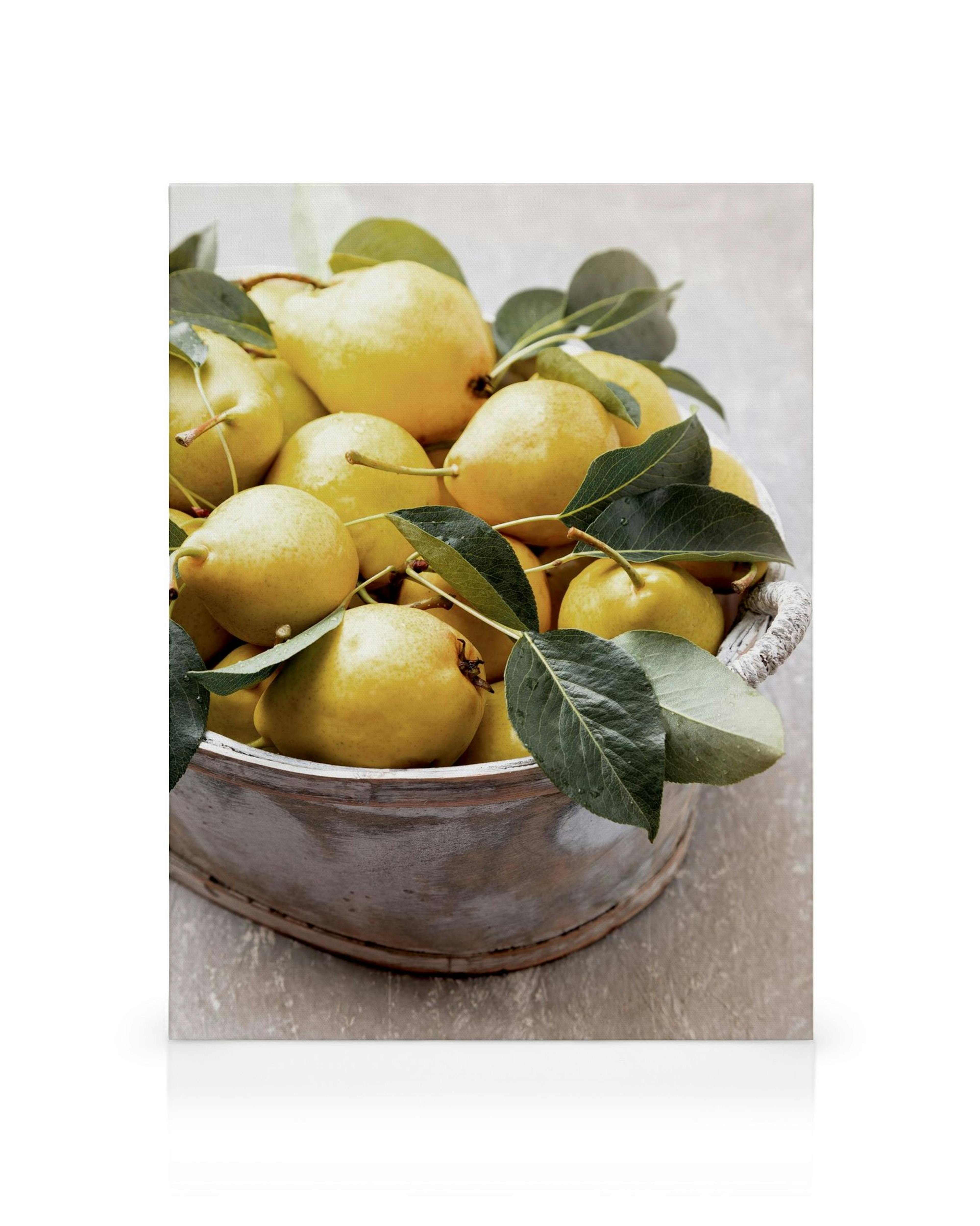 Leinwandbild mit gelben Sommerbirnen und grünen Blättern in rustikaler Holzschale