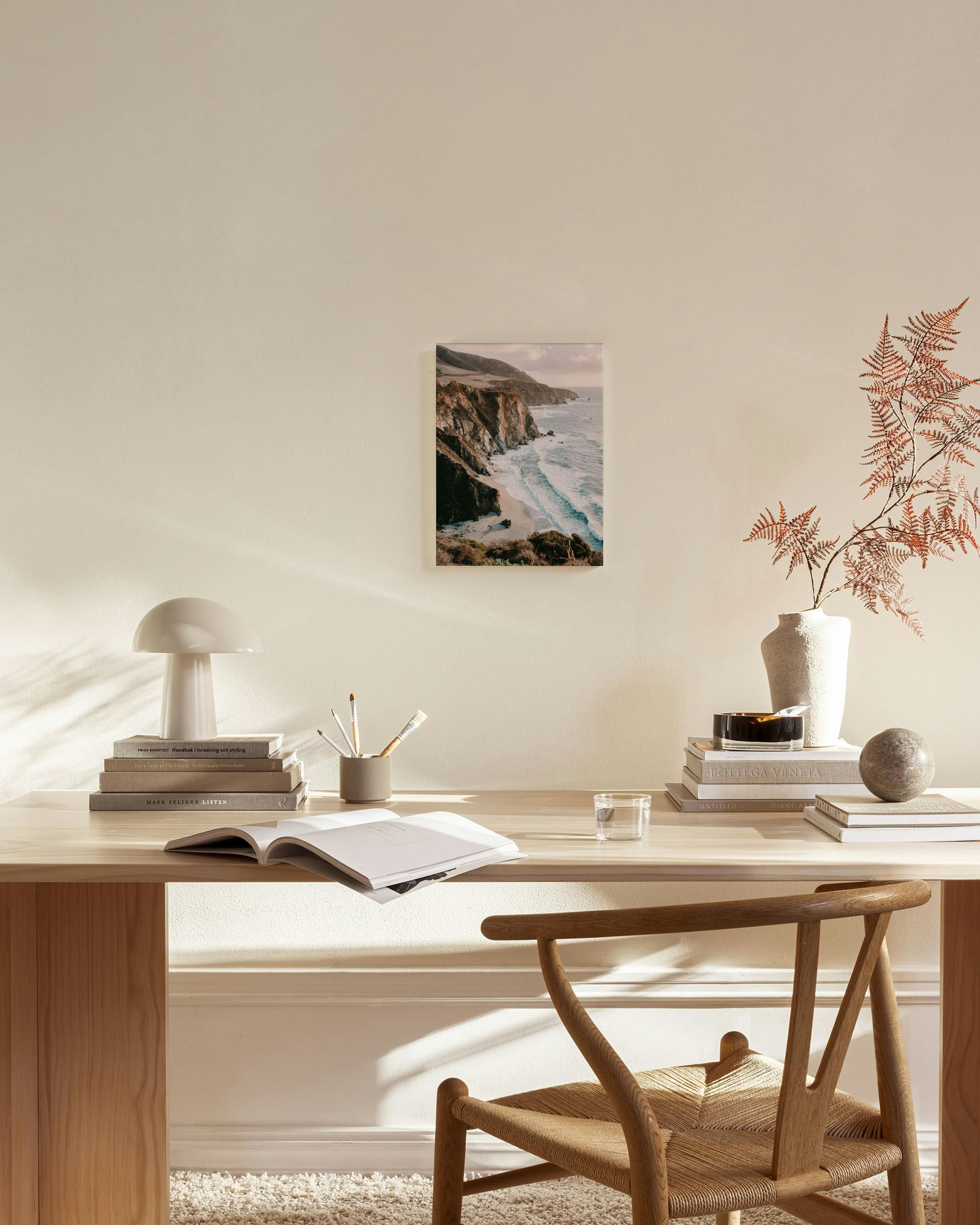 Καμβάς με βραχώδη ακτογραμμή και γαλάζια κύματα, κρεμασμένος σε μίνιμαλ σαλόνι πάνω από ξύλινο μπουφέ.