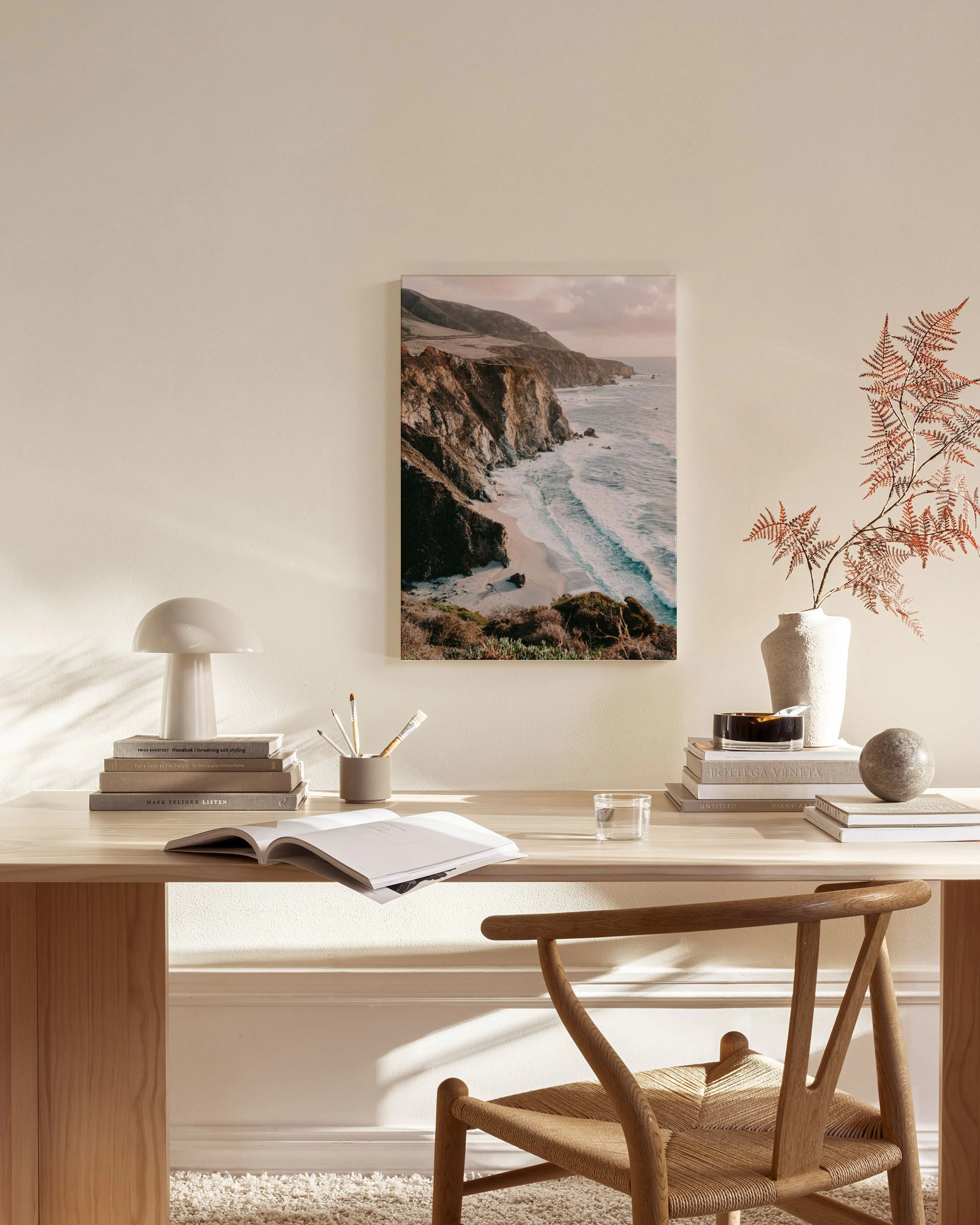 Canvas met rotsachtige kustlijn en golvende zee, hangend in een lichte woonkamer boven een houten dressoir.
