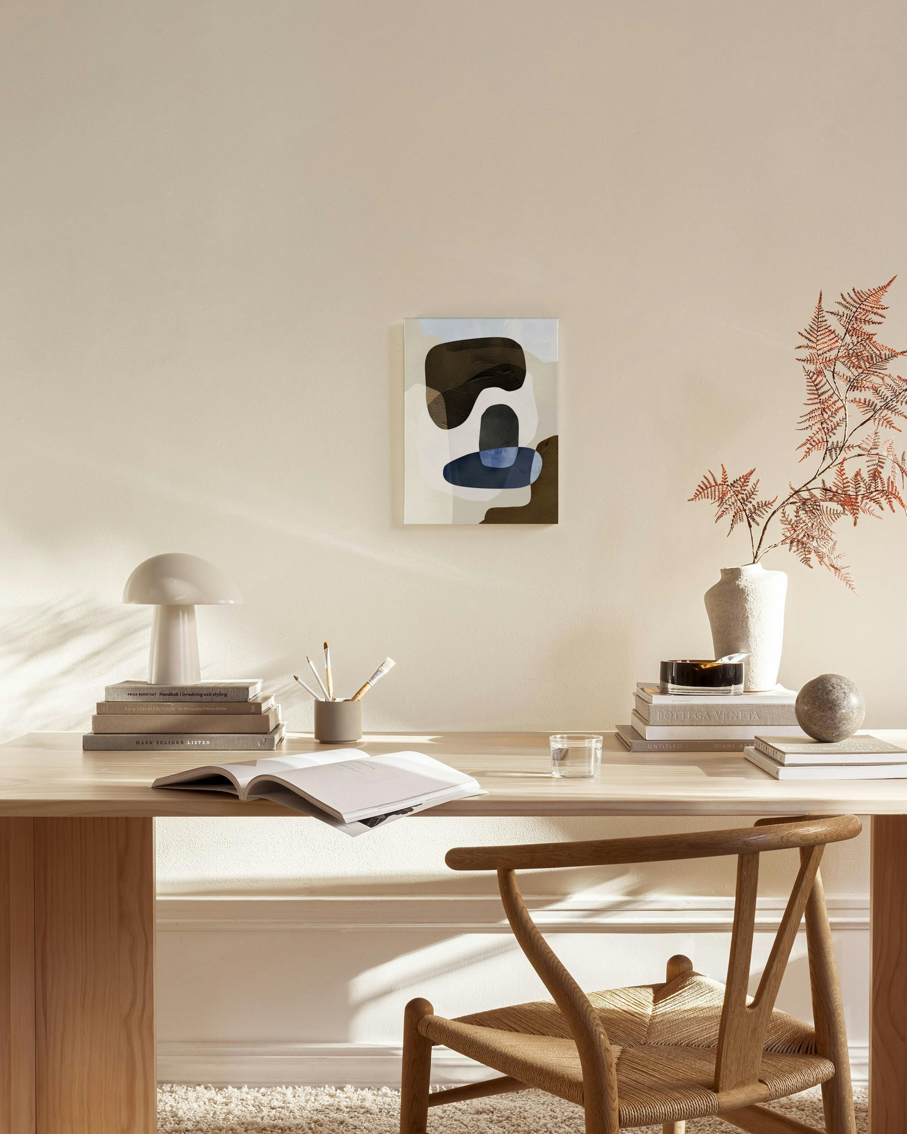 Obraz na plátně s hnědými, modrými a béžovými organickými tvary, visící nad dřevěnou komodou v moderním obývacím pokoji.