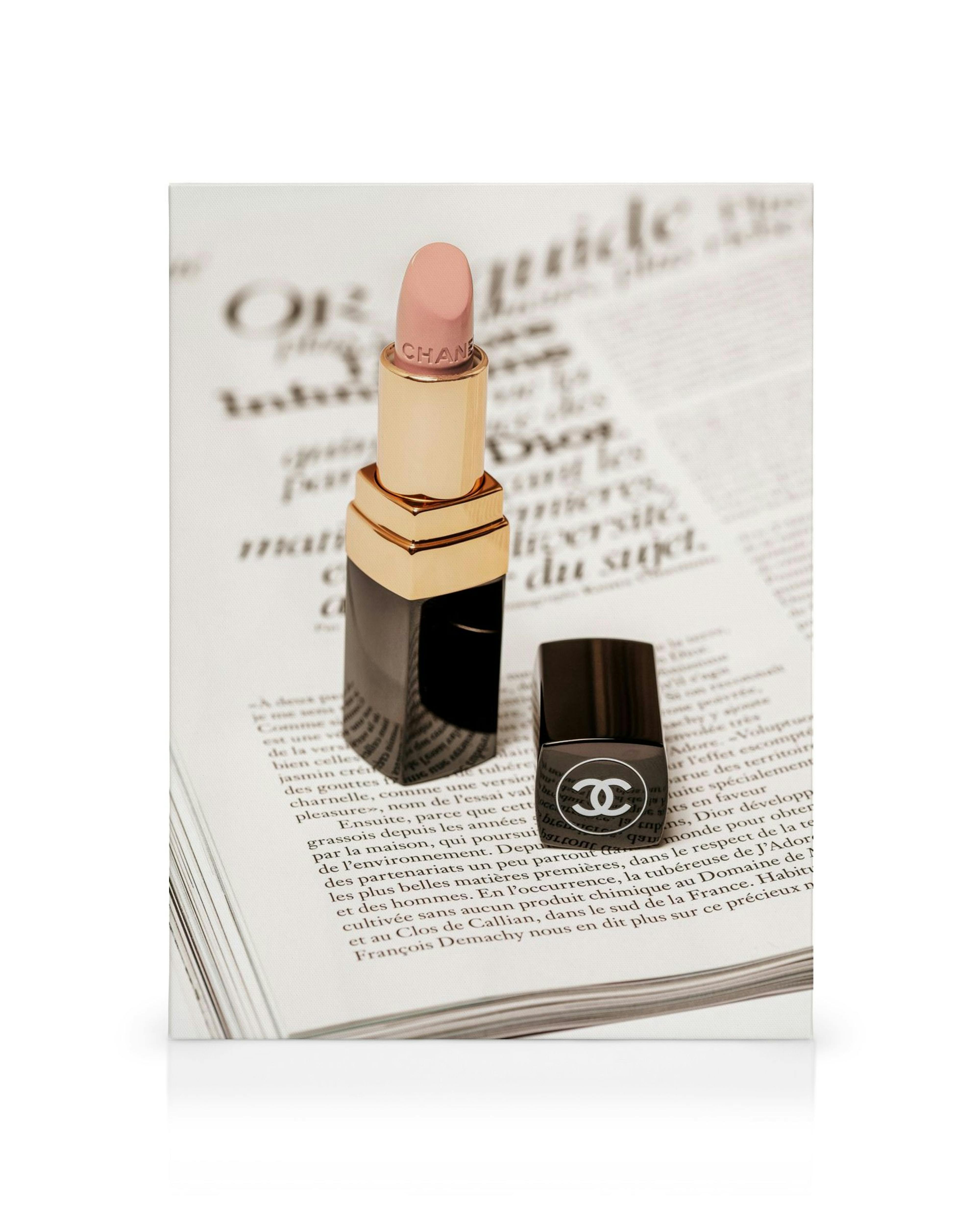 Chanel lipstick canvas print with black and gold lipstick and pink tip on an open magazine, next to a black nail polish bottle.