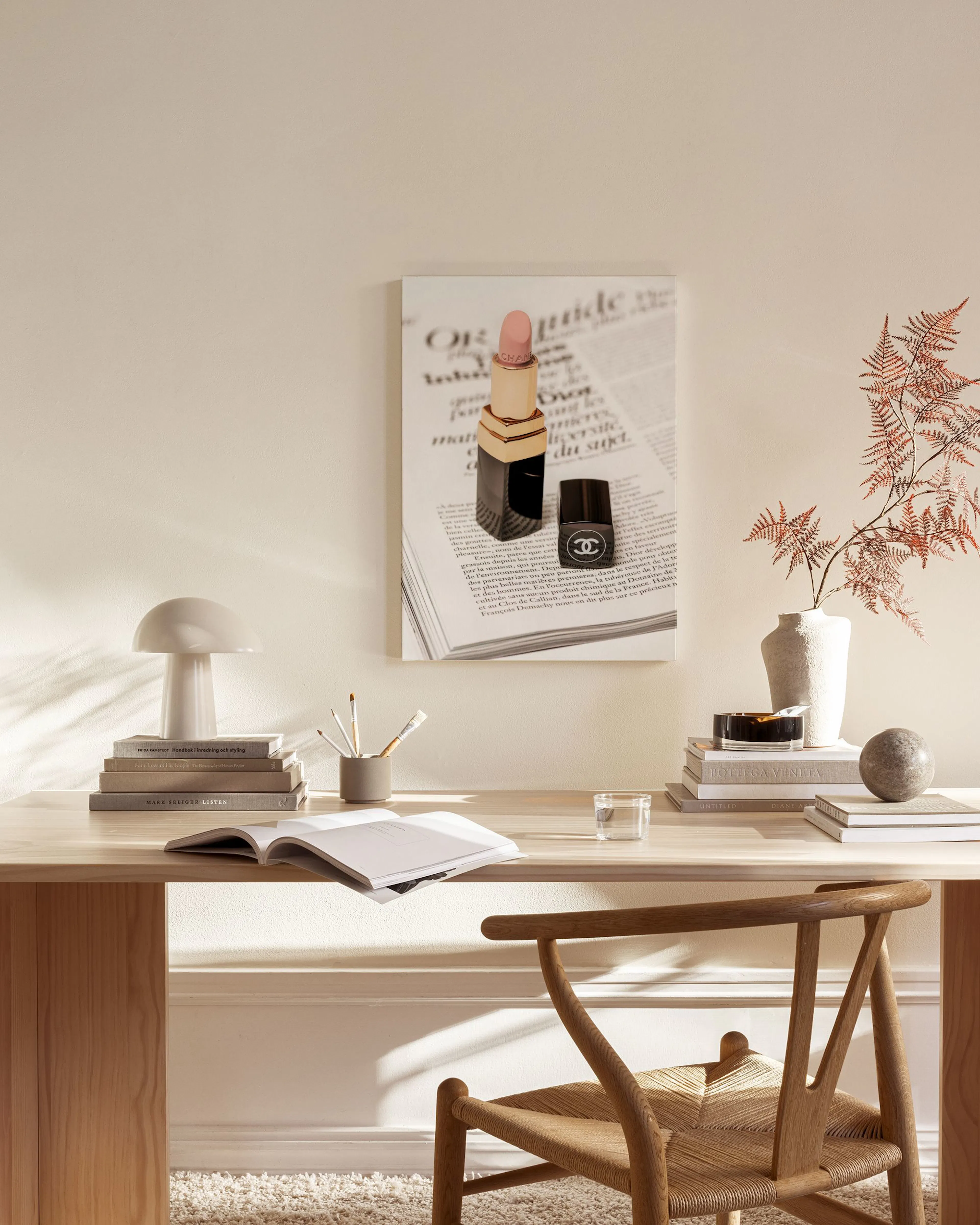 Leinwandbild mit Lippenstift und Parfümflakon auf Zeitungsseite, hängend in einem hellen Wohnzimmer über einem Sideboard.