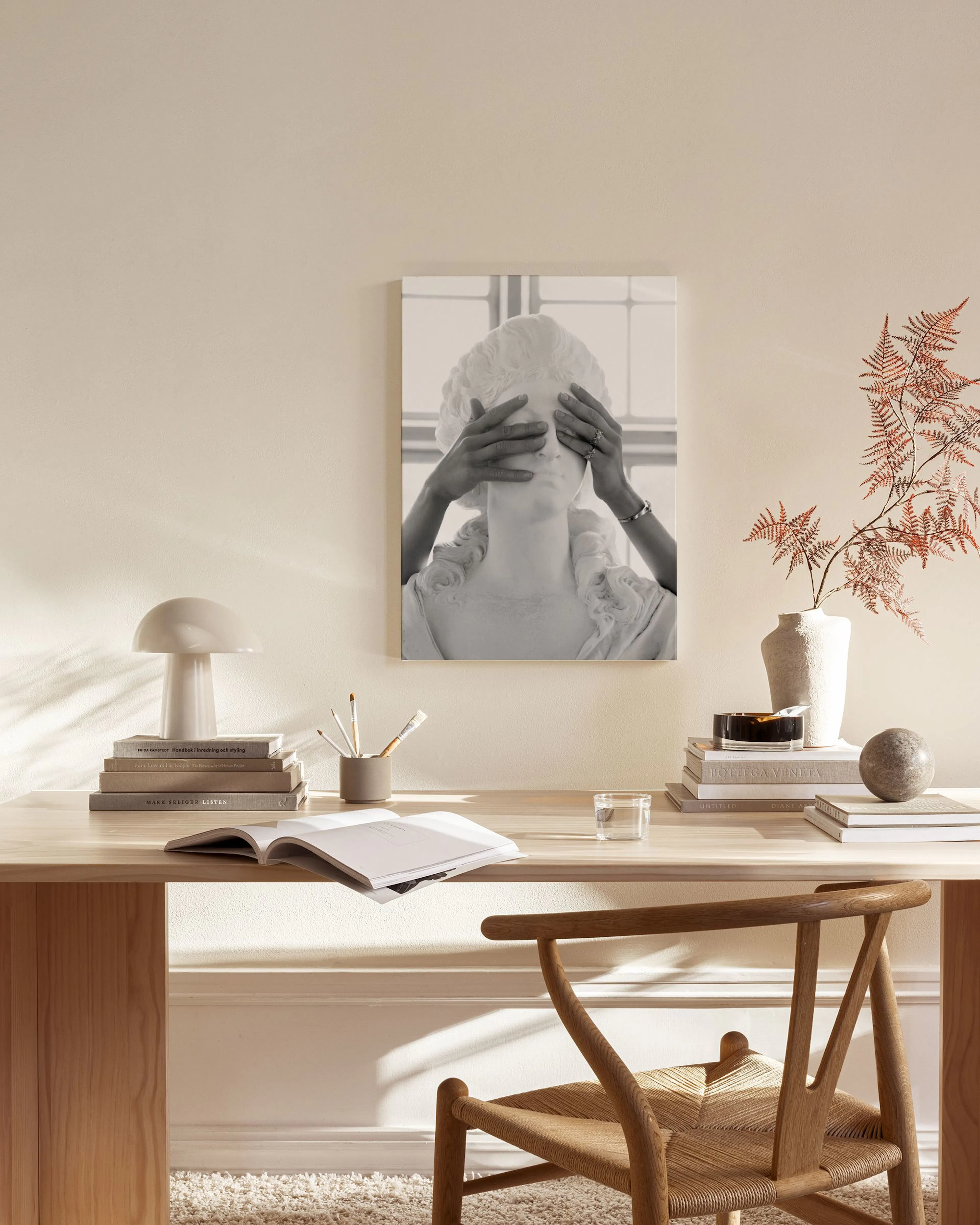 Schwarz-weißes Leinwandbild einer Statue, deren Augen von Händen bedeckt sind, in einem hellen Wohnzimmer über einem Sideboard.