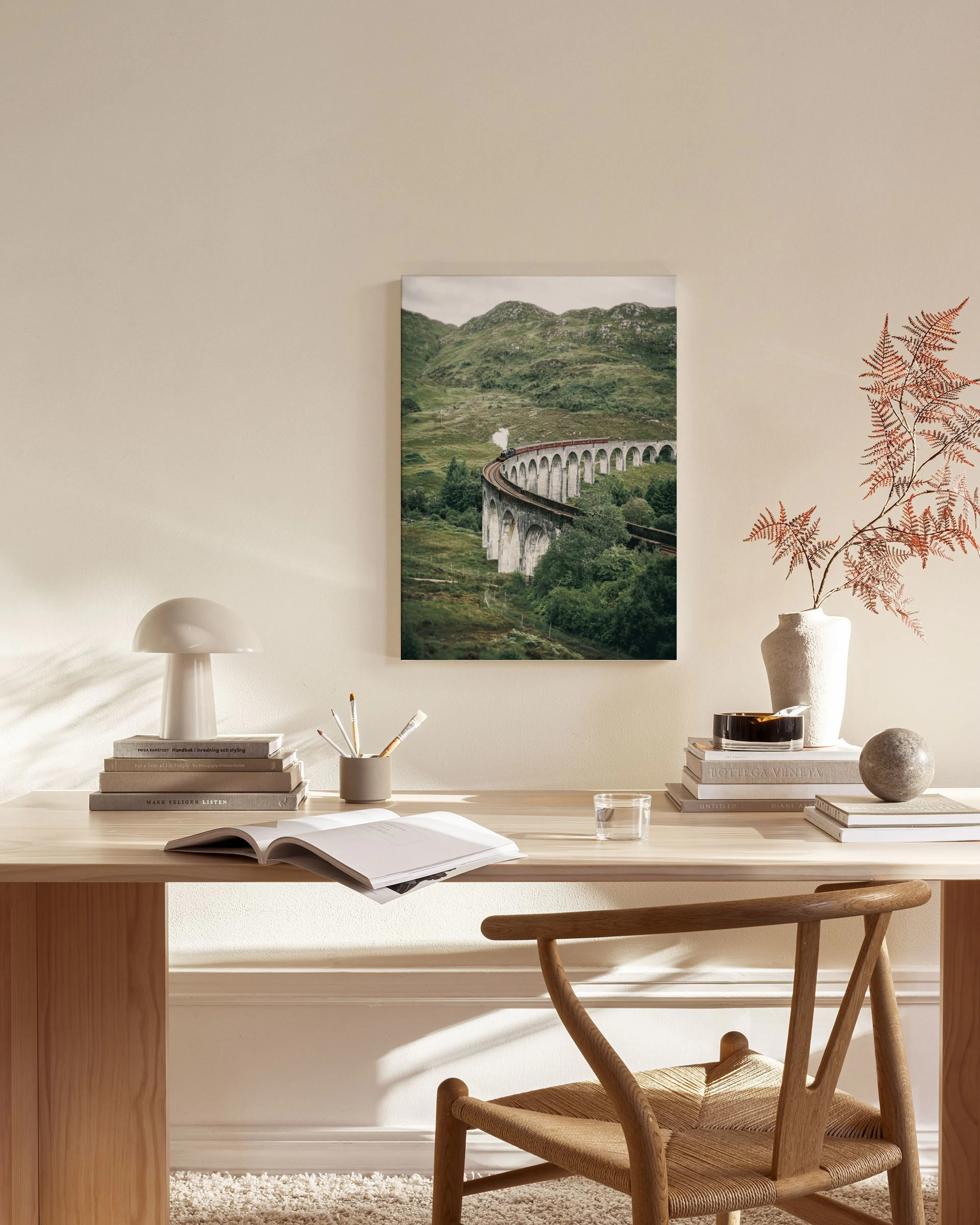 Canvastavla med tåg på viadukt i grönskande landskap, hängandes ovanför bänk med inredning i ett vardagsrum.