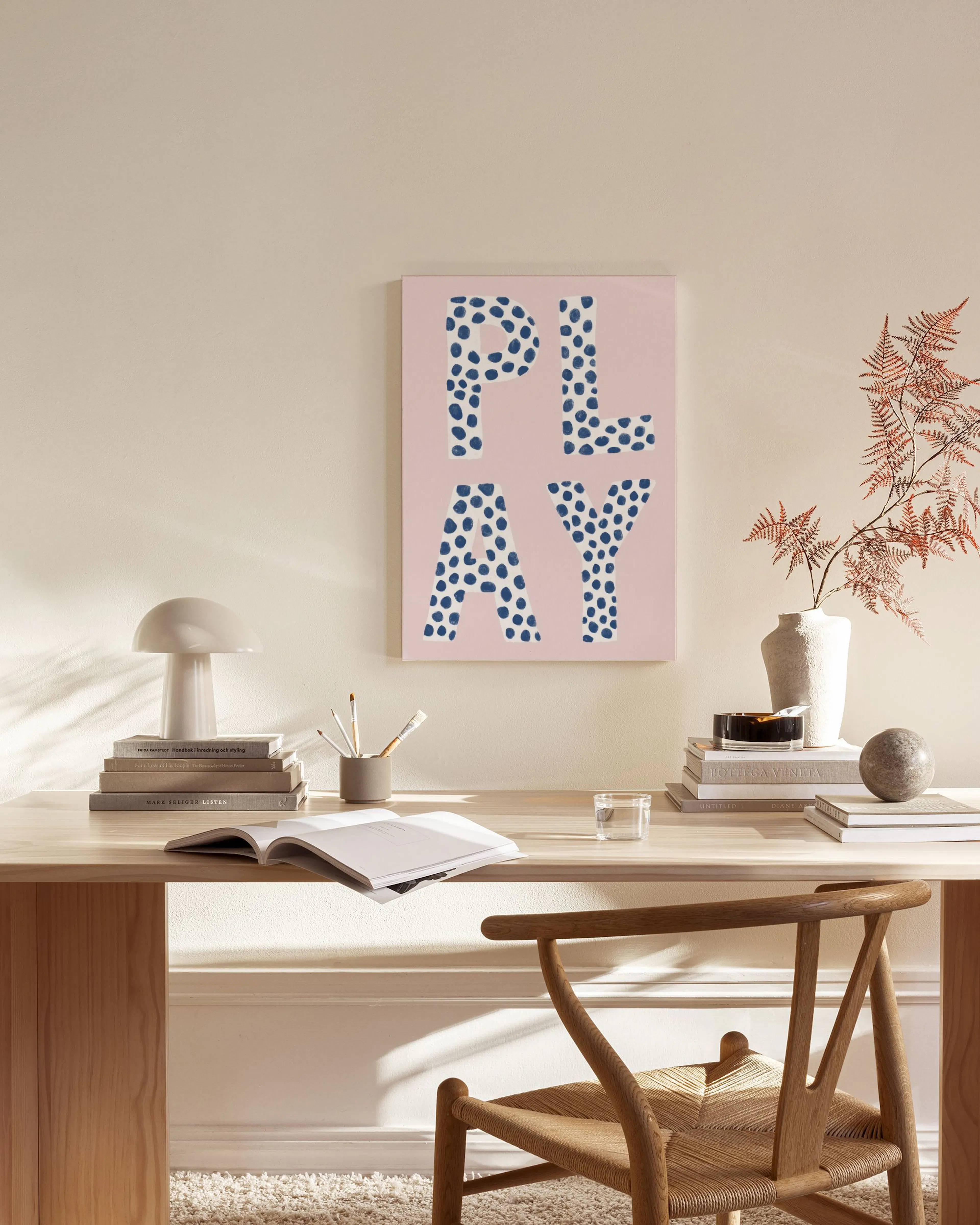 Toile rose avec le mot PLAY en lettres bleues à pois, affichée dans un salon moderne aux tons neutres.