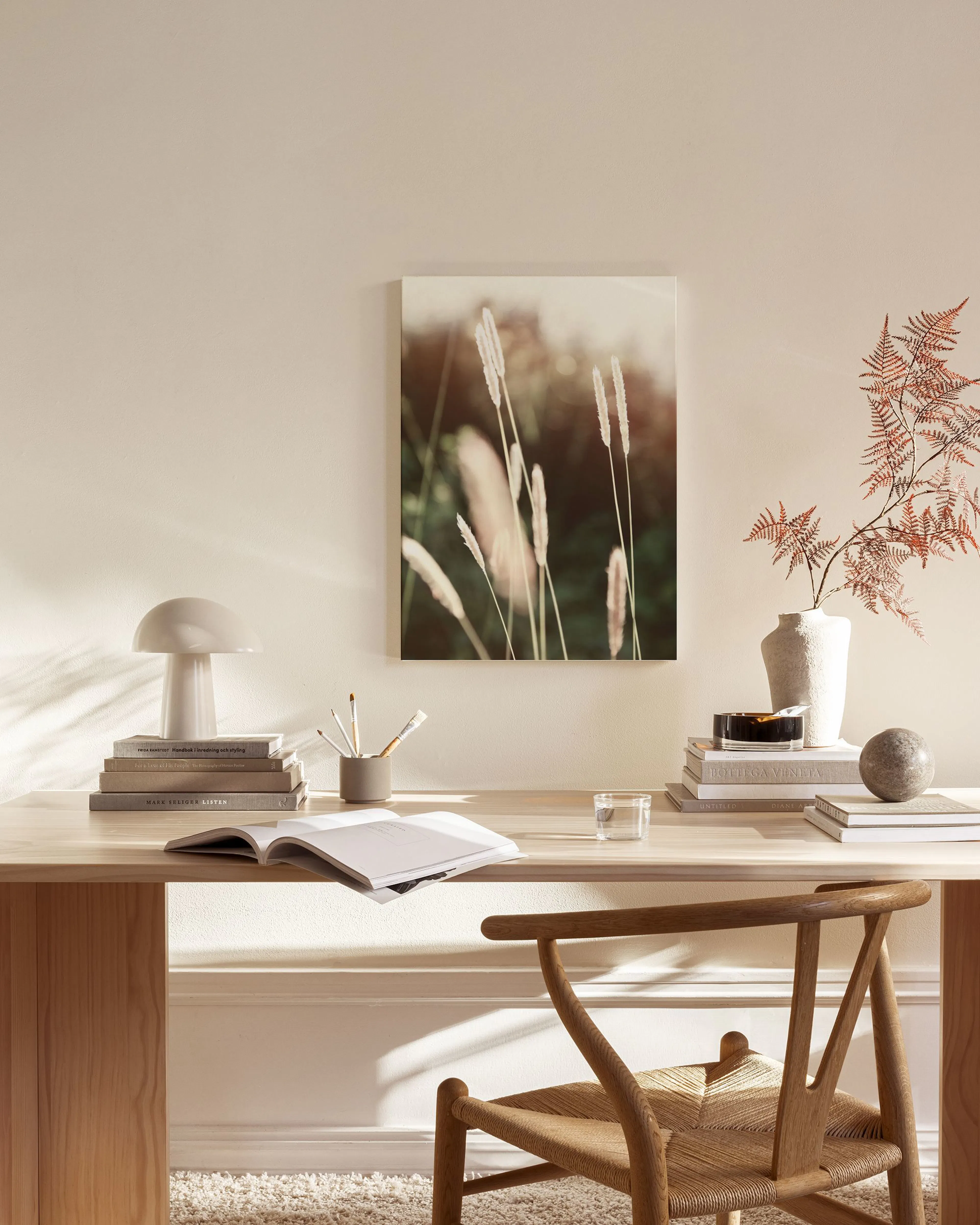 Canvas met pluimgras in een zachtgroene omgeving, hangend boven een houten dressoir in een lichte woonkamer.