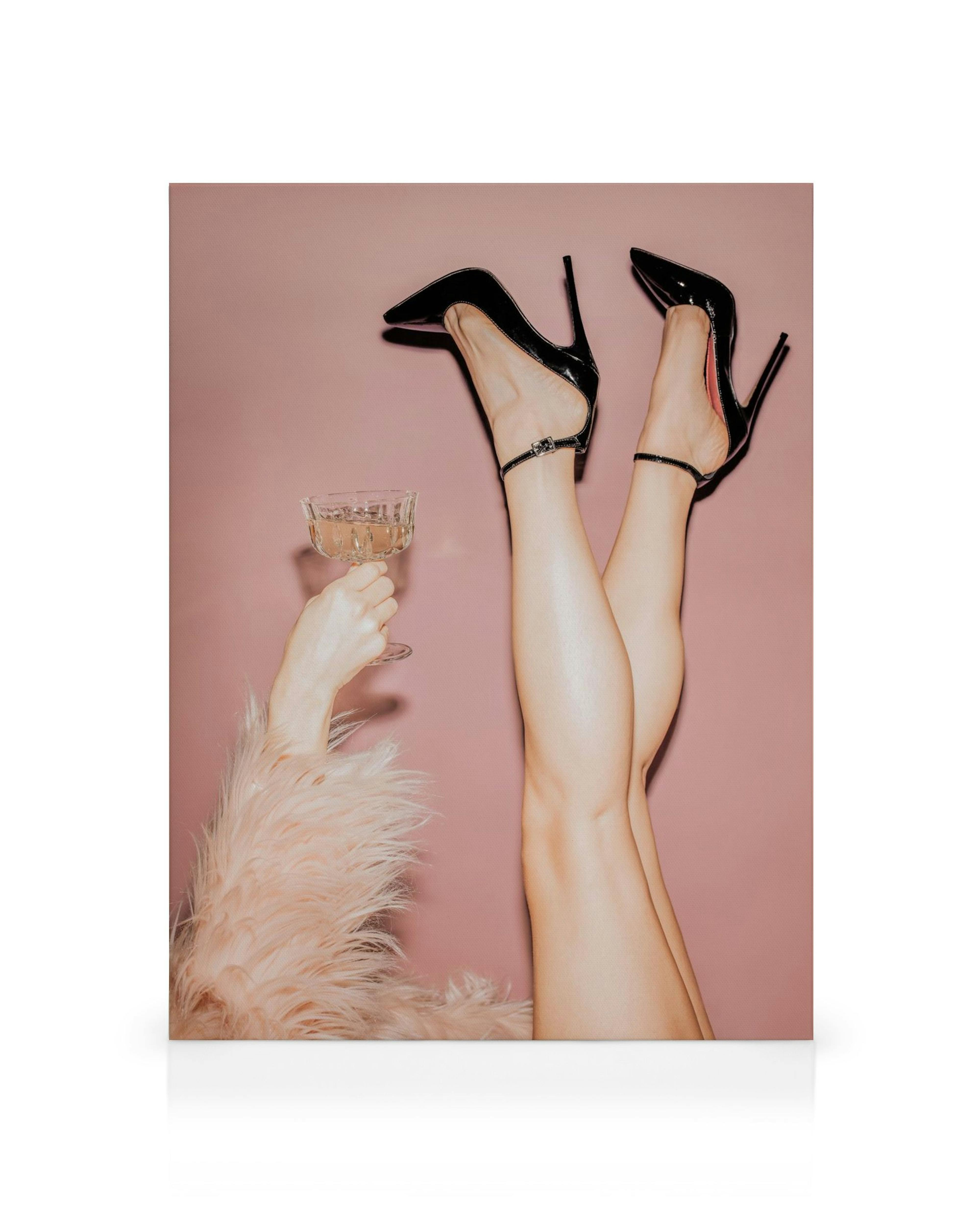 Nohy v čiernych lodičkách a ruka s pohárom šampanského na ružovom pozadí