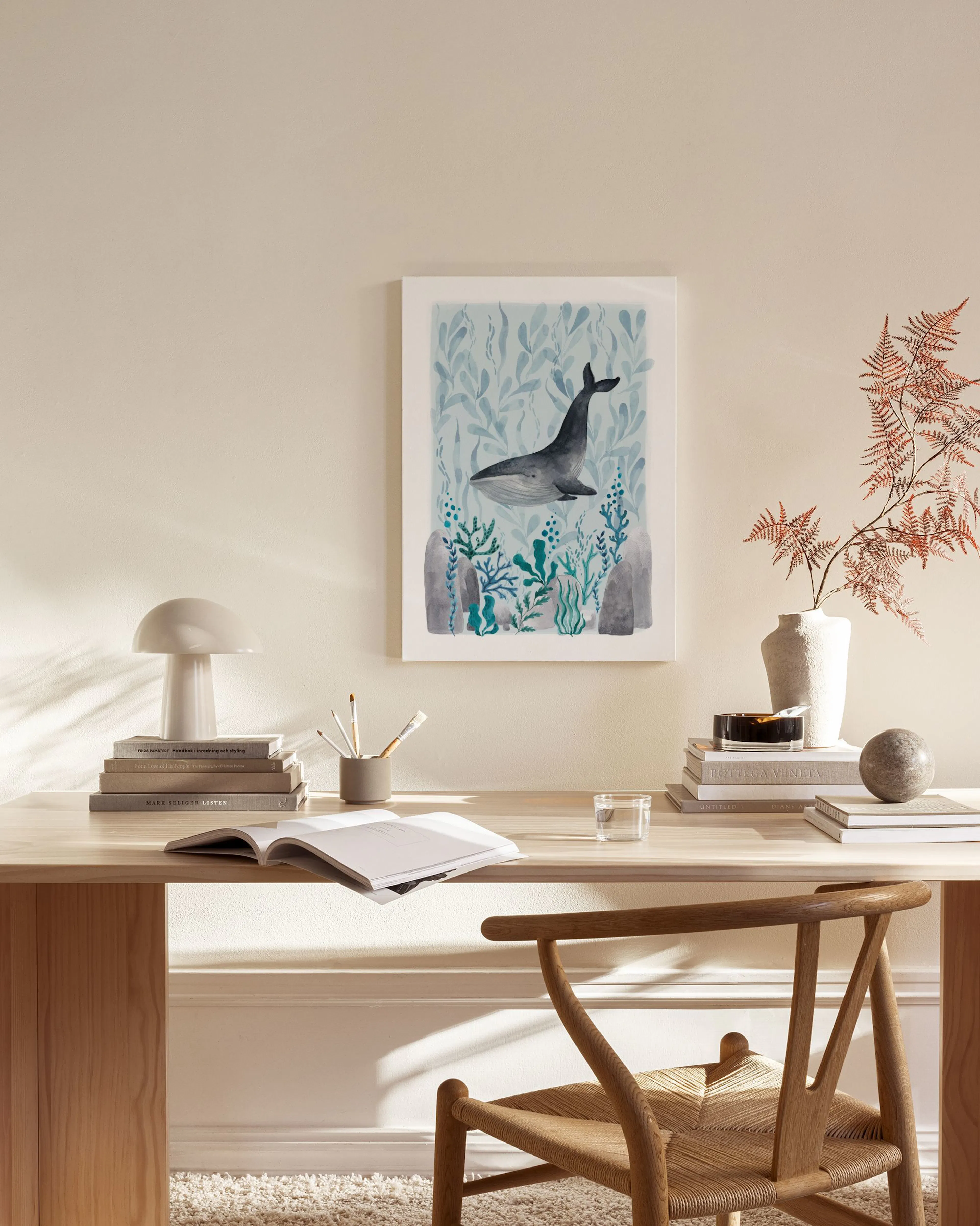 A watercolor print of a grey whale swimming in blue and green underwater foliage, hanging in a minimalist living room.