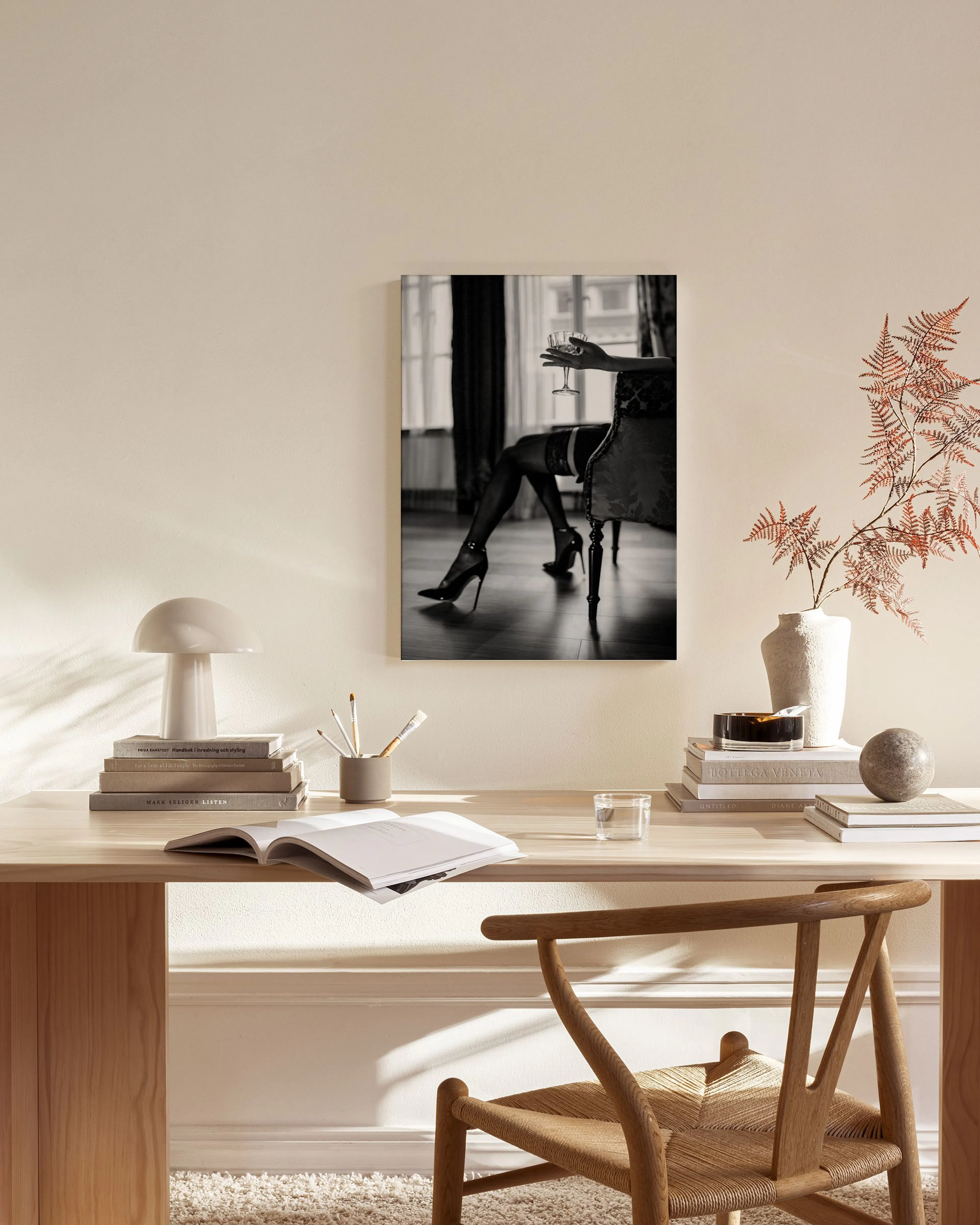 Zwart-wit canvas van een vrouw in hoge hakken en kousenbanden met een glas, hangend in een moderne woonkamer.