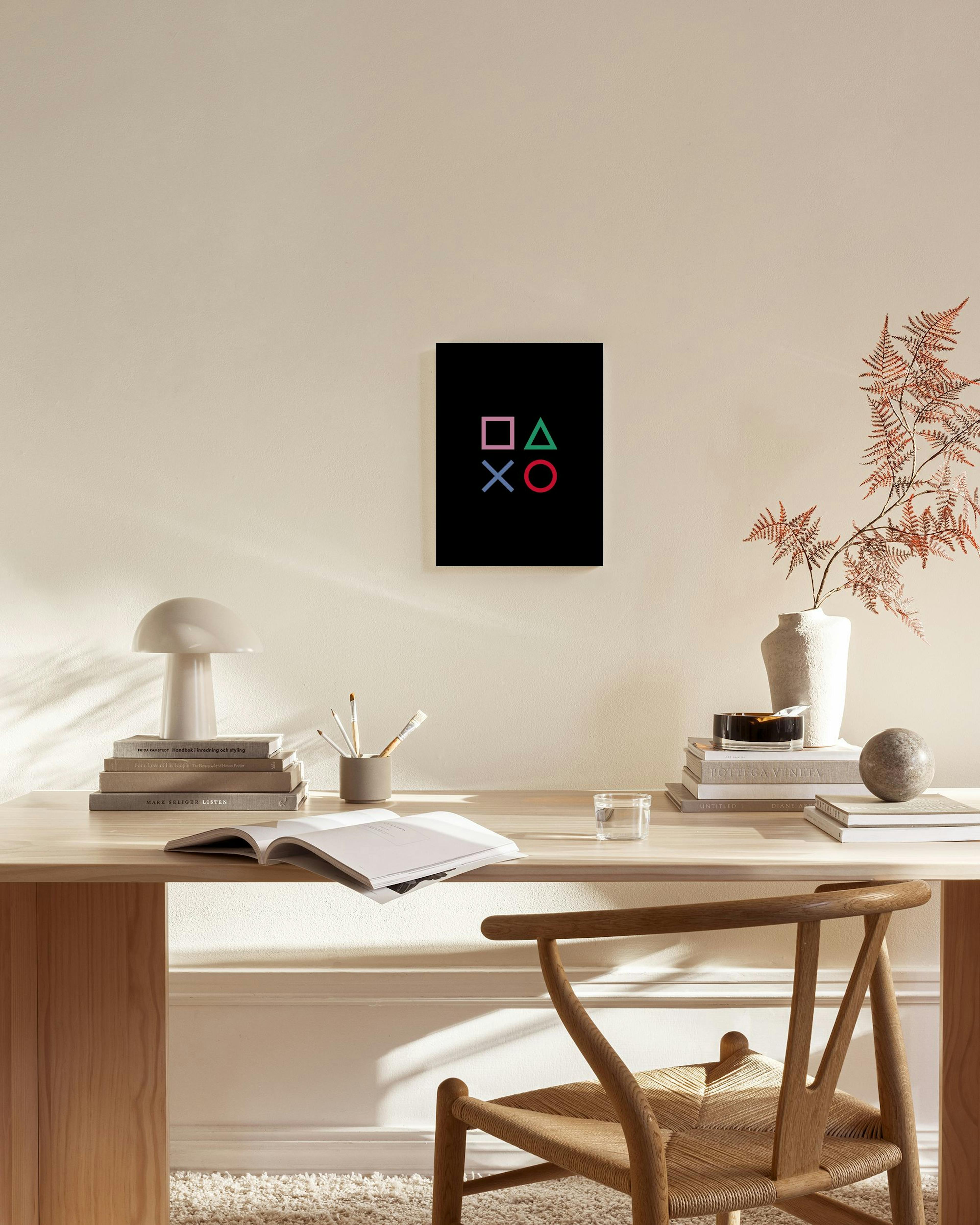 A PlayStation symbols canvas print with pink square, green triangle, blue X, and red circle on a black background, hanging in a 