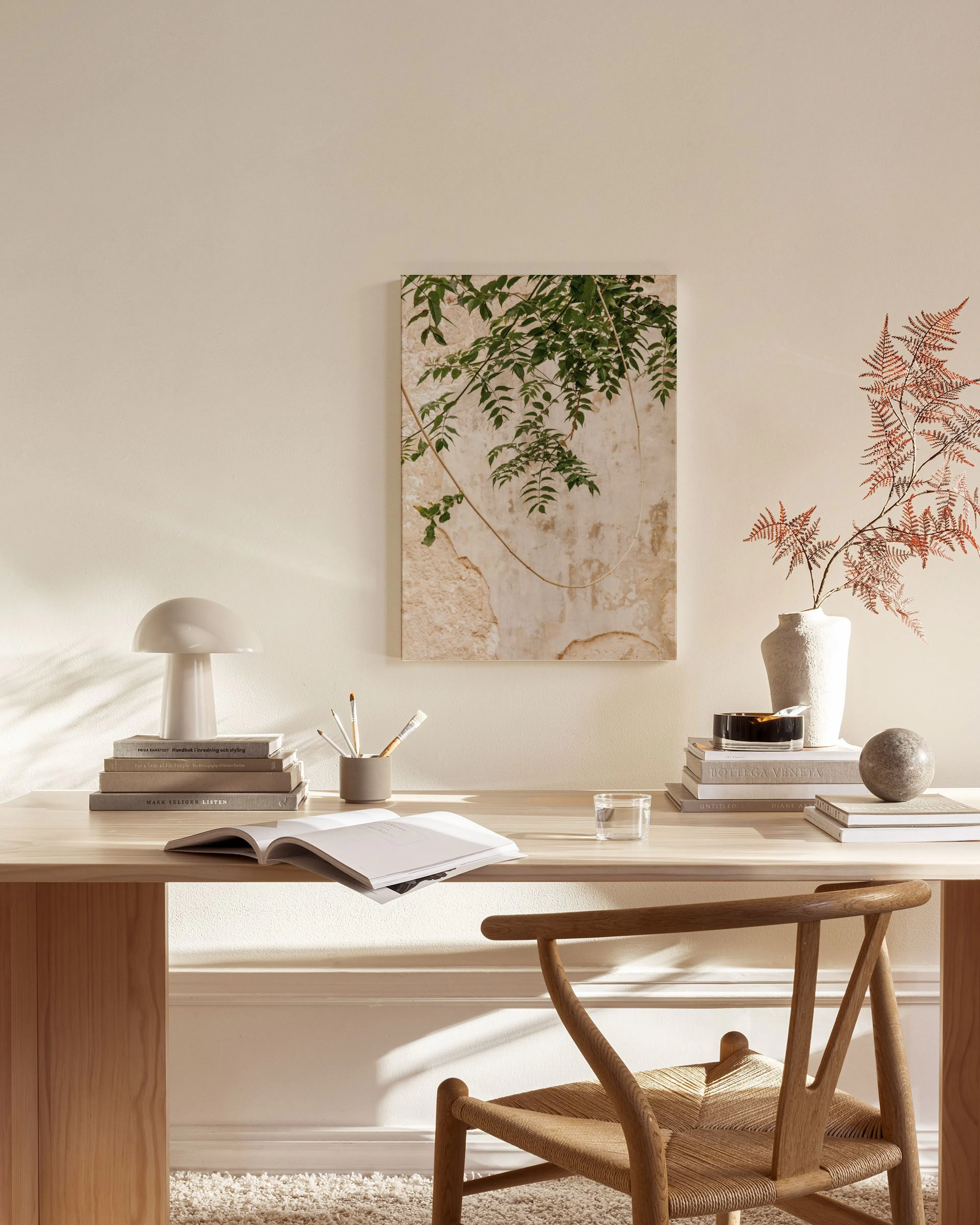 Leinwandbild mit dunkelgrünen Blättern vor einer beigefarbenen, rissigen Wand, hängend in einem hellen Wohnzimmer.