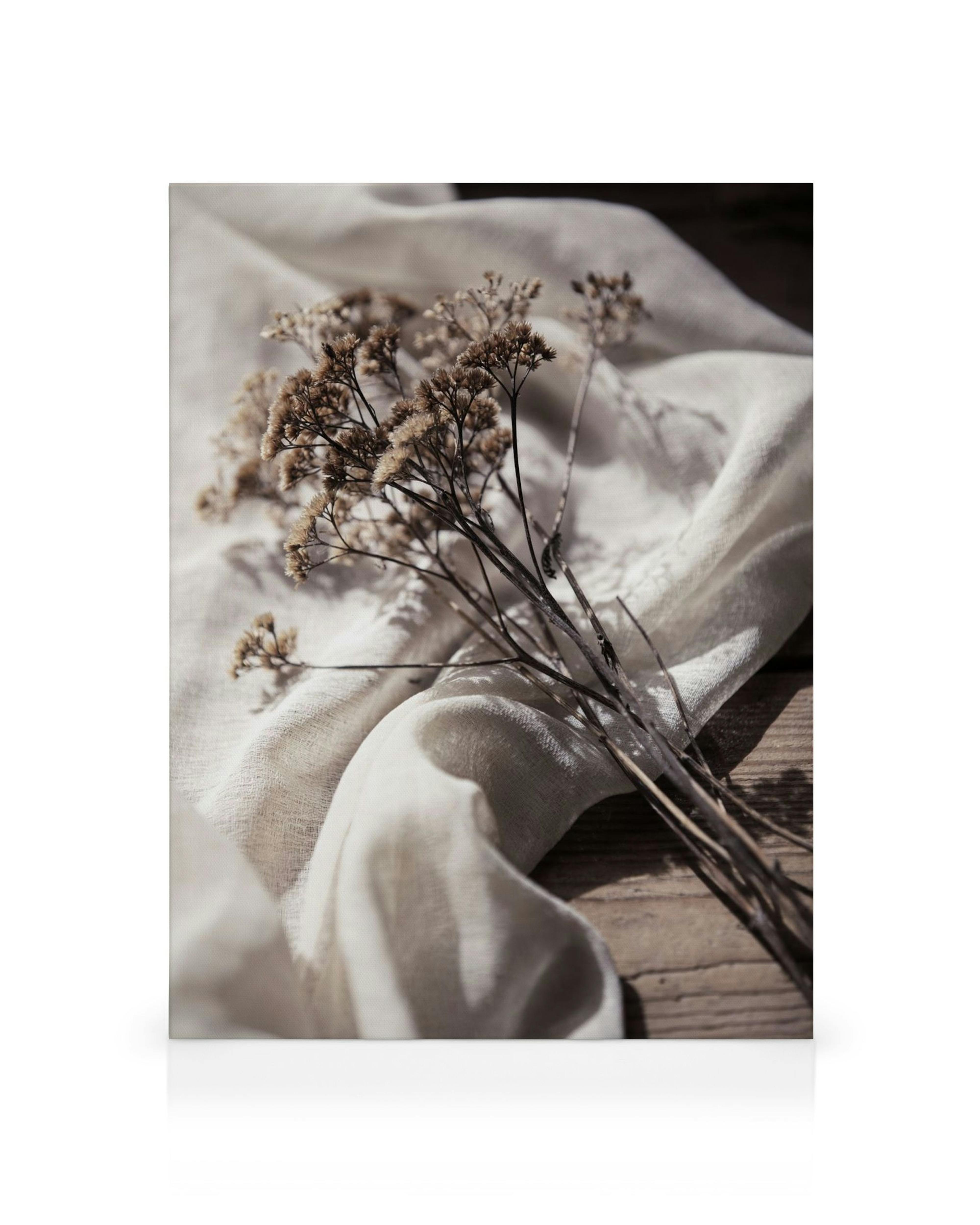 Leinwandbild mit getrockneten Blumen auf beigem Stoff, rustikaler Holzuntergrund, natürliche Sepia-Töne