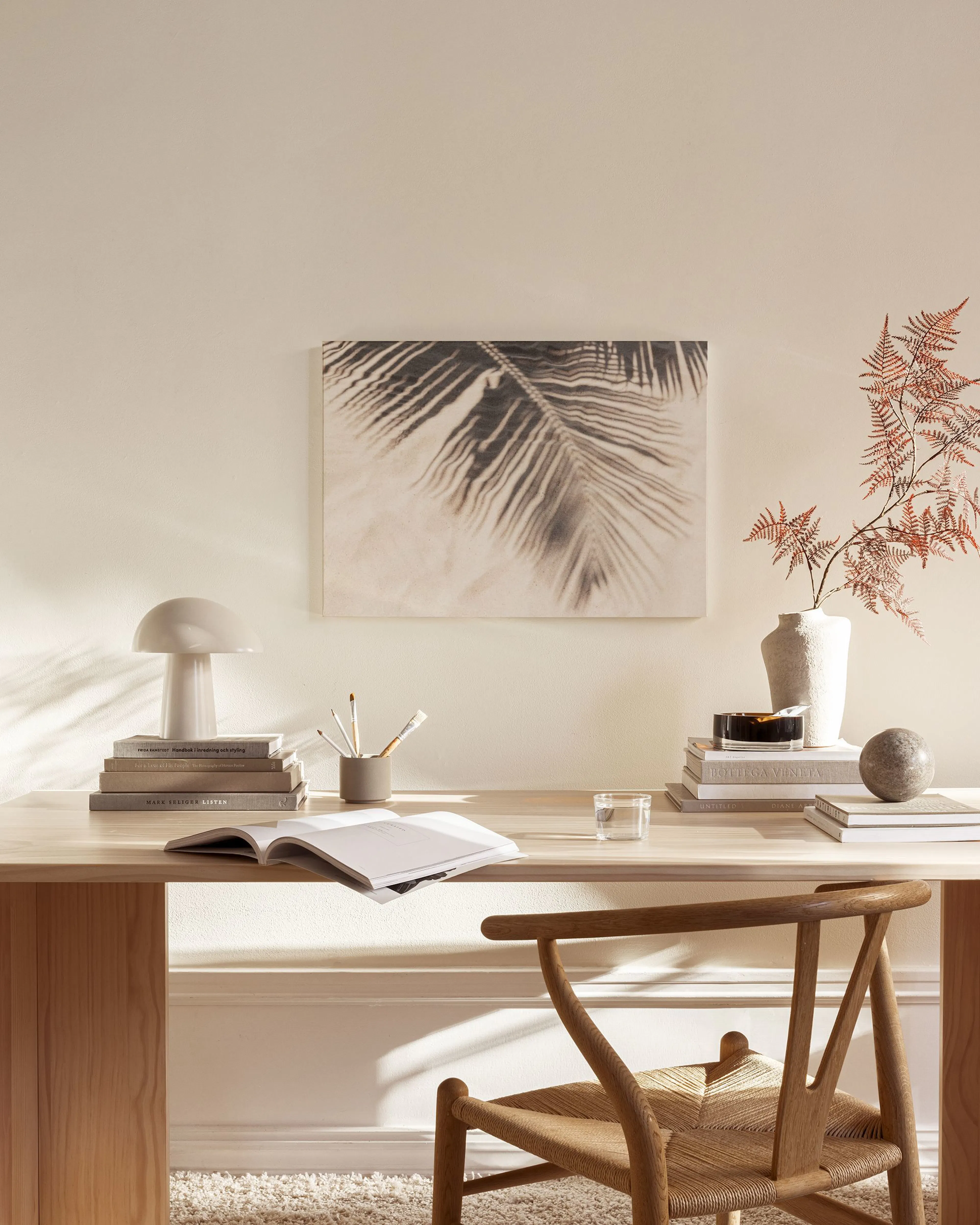 A sepia canvas print of a palm leaf on sand, hanging above a wooden cabinet in a Scandinavian-style living room.