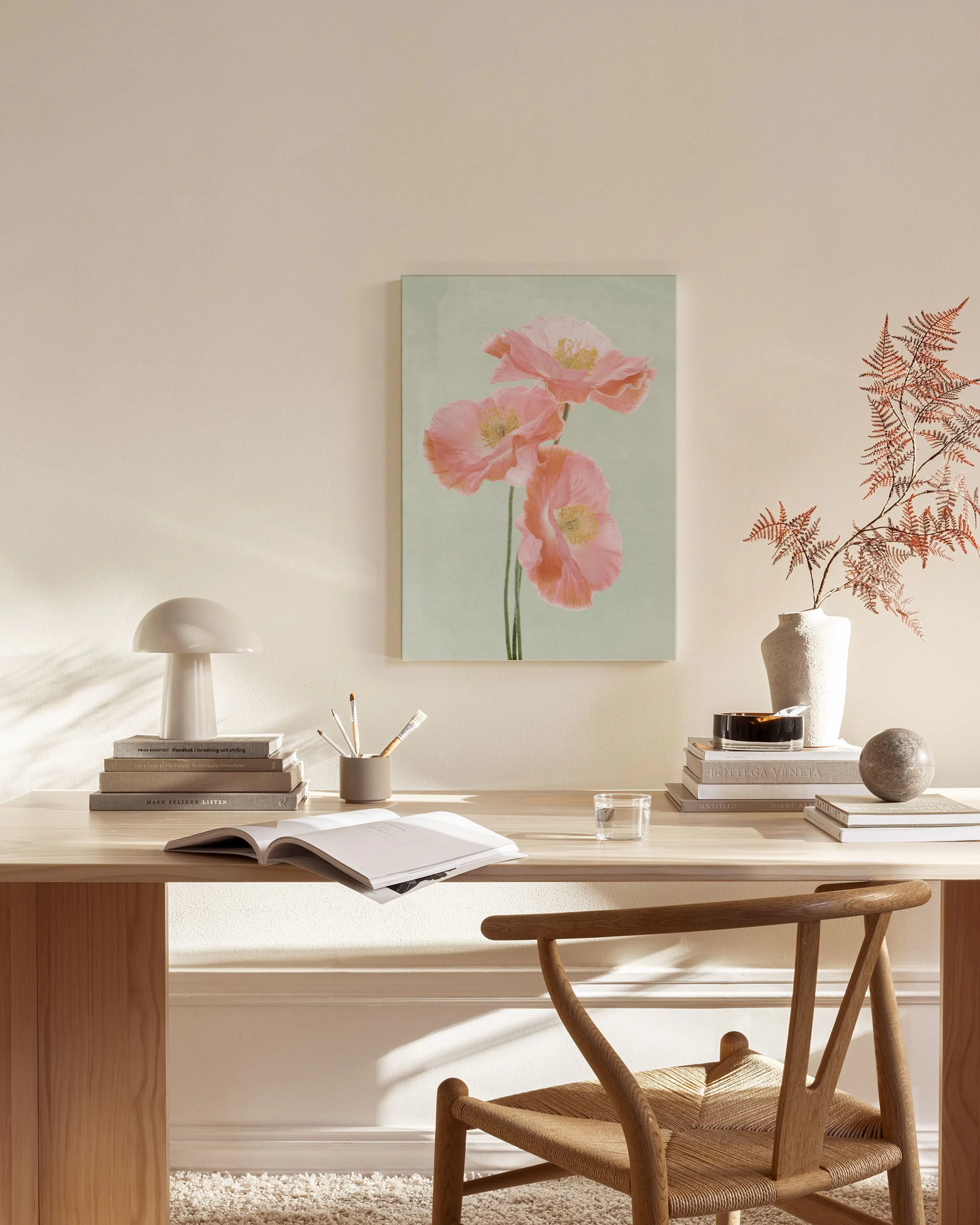 A canvas print of three delicate pink poppies on a soft green background, displayed in a bright, minimalist living room.