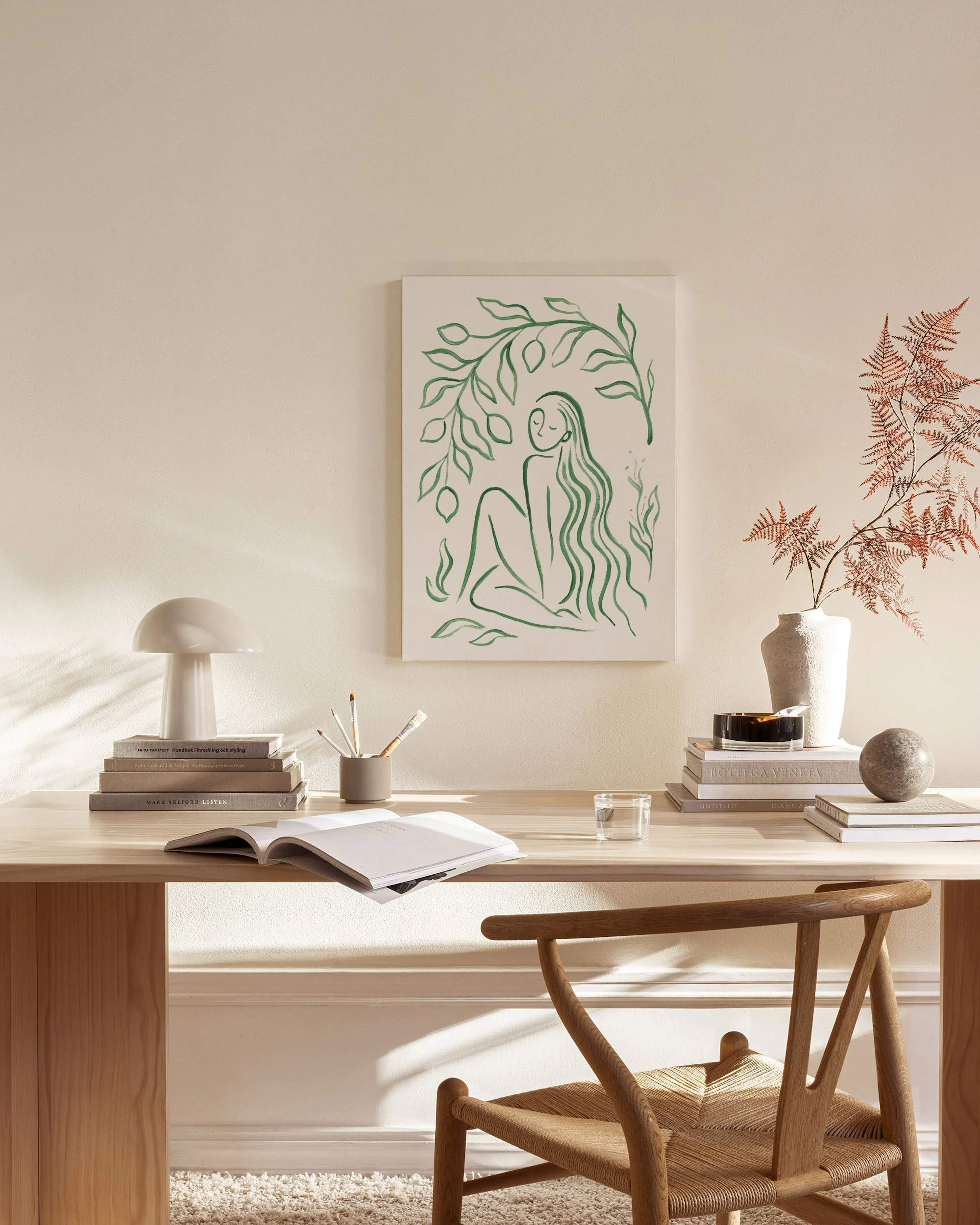 Stampa su tela con figura femminile verde e rami di limone, appesa sopra una panca in un salotto moderno.