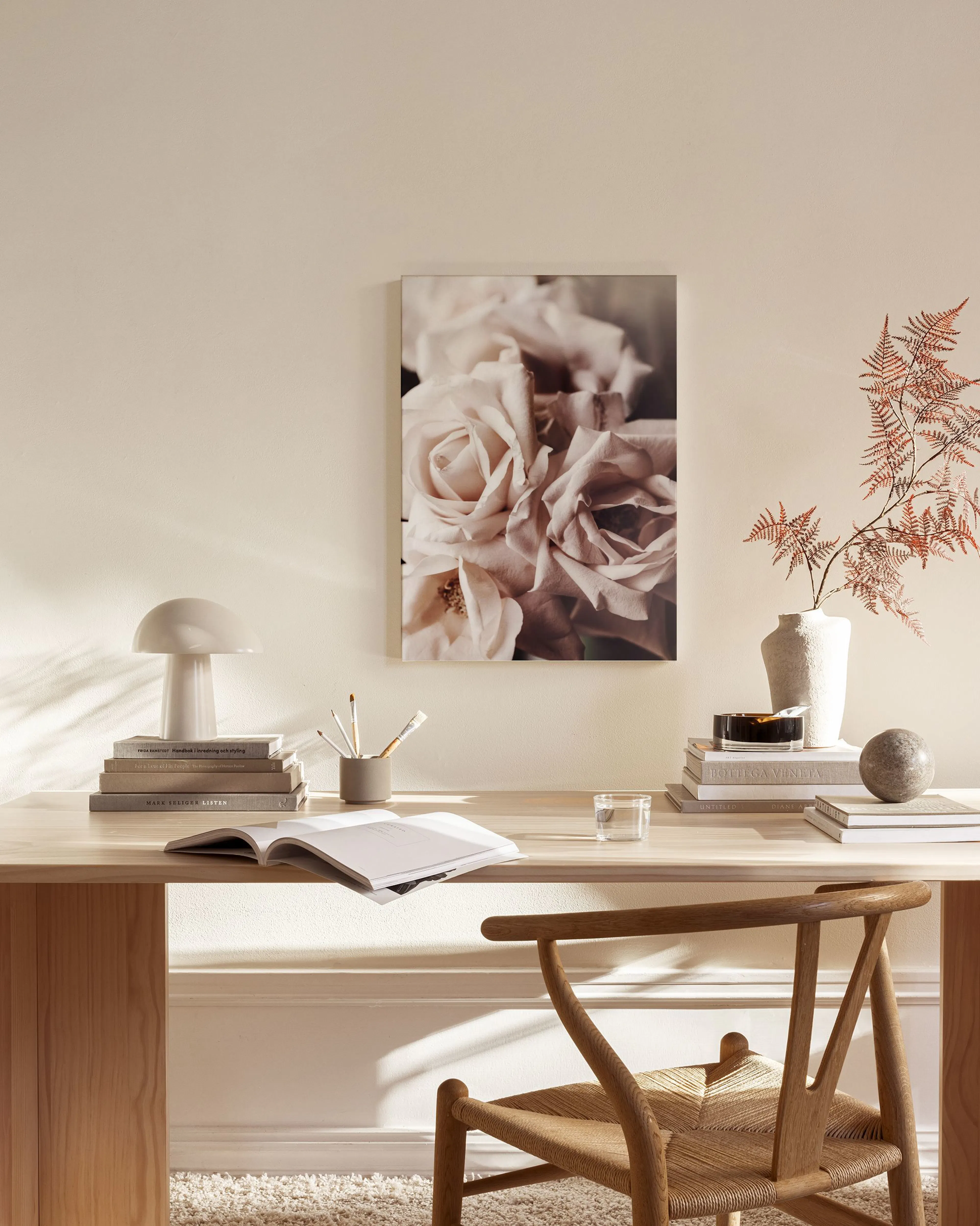 A canvas print of soft pink roses in bloom, hanging above a wooden console table in a minimalist living room.