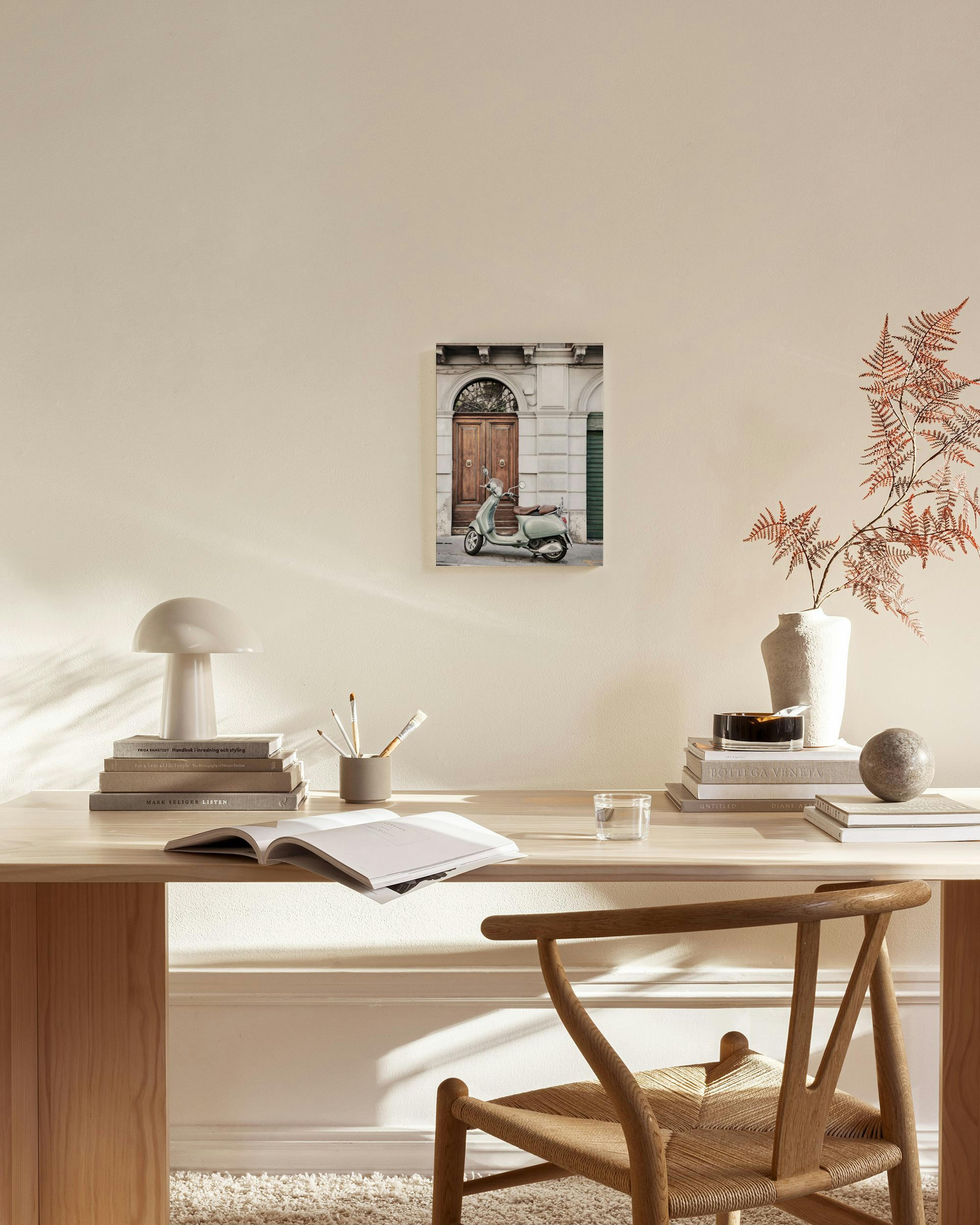 A canvas print of a light green vintage scooter parked in front of a rustic wooden door, hanging in a minimalist living room.