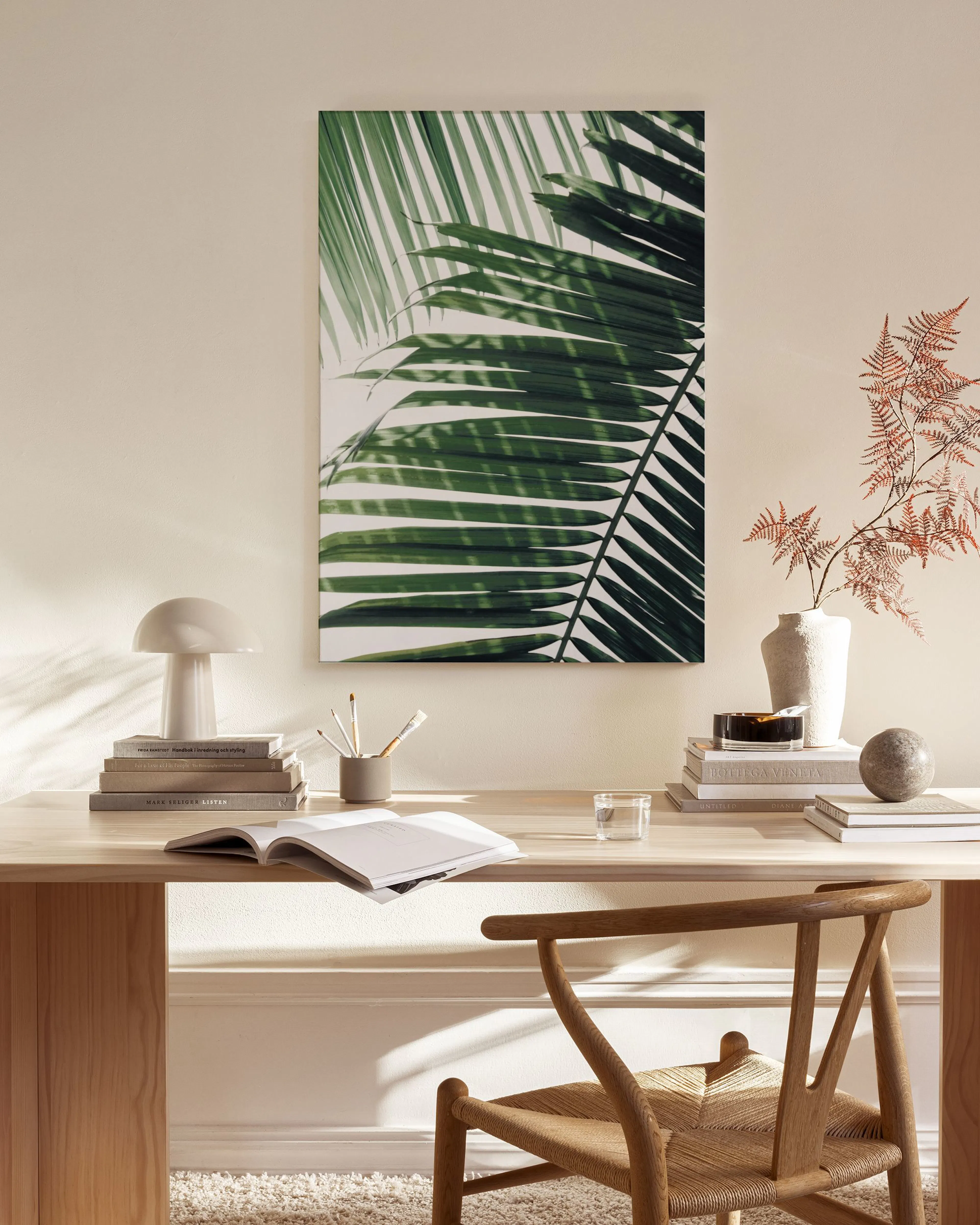 Leinwandbild mit Palmenblattmotiv, über einem Sideboard in einem hellen Wohnzimmer mit Sessel und Couchtisch.